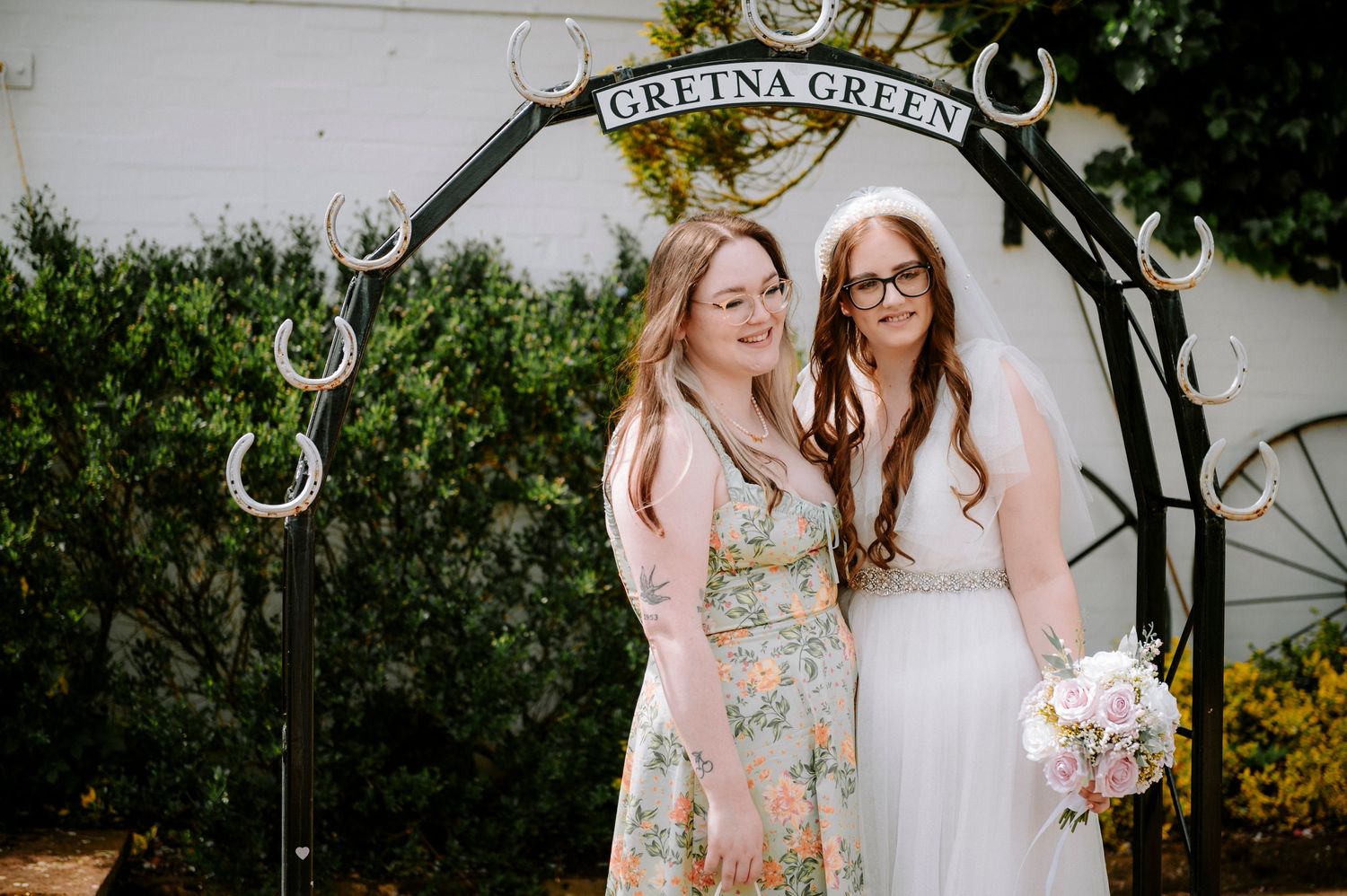 Two people posing under the Gretna Green horseshoe arch on a sunny day.