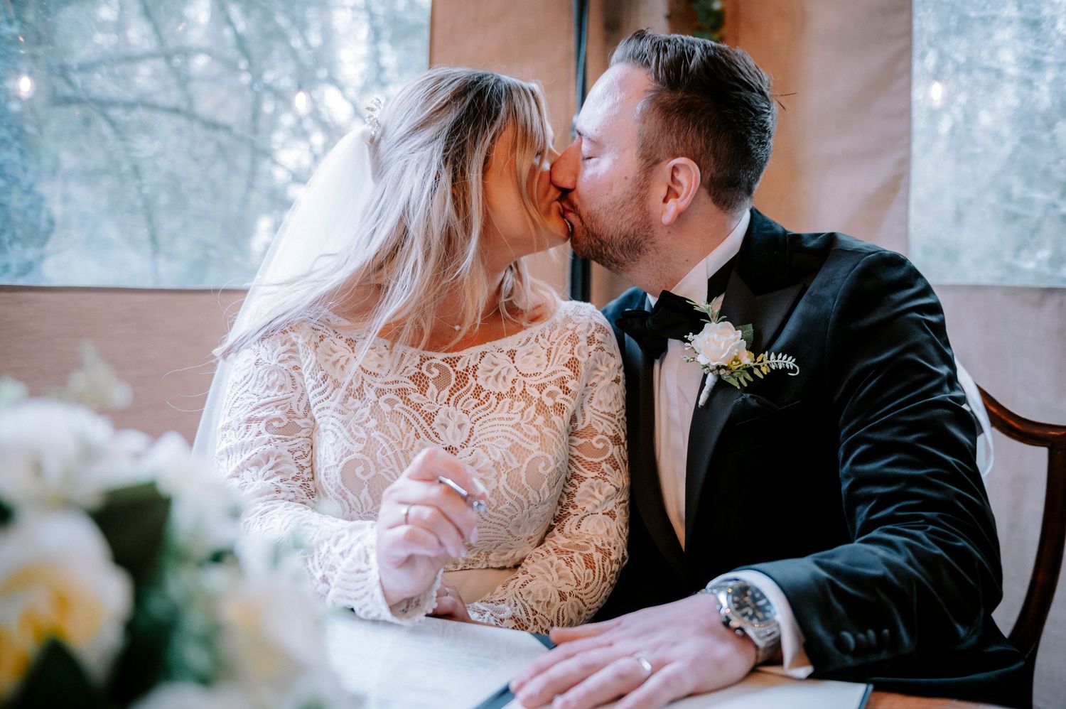 Tender wedding moment captured in a rustic venue with snow-covered windows in background.