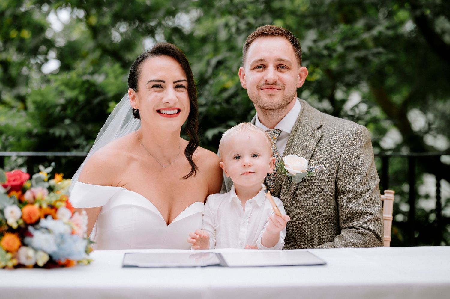 Joyful wedding ceremony signing moment with baby and floral decorations.