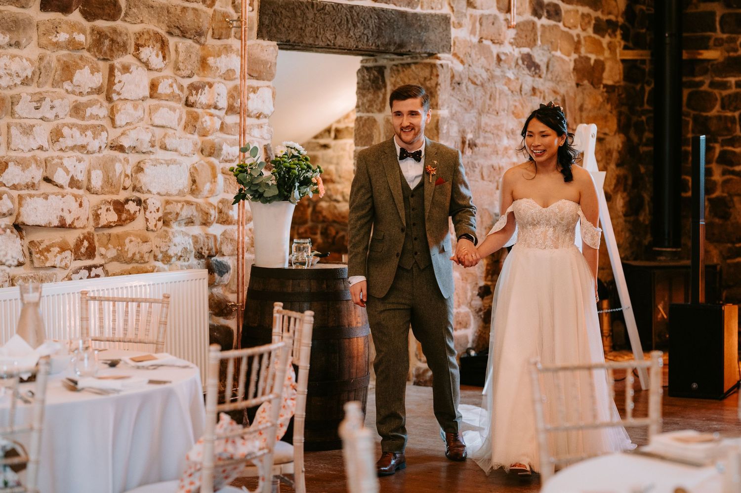 A wedding couple makes their entrance into a rustic stone-walled reception venue with elegant table settings.