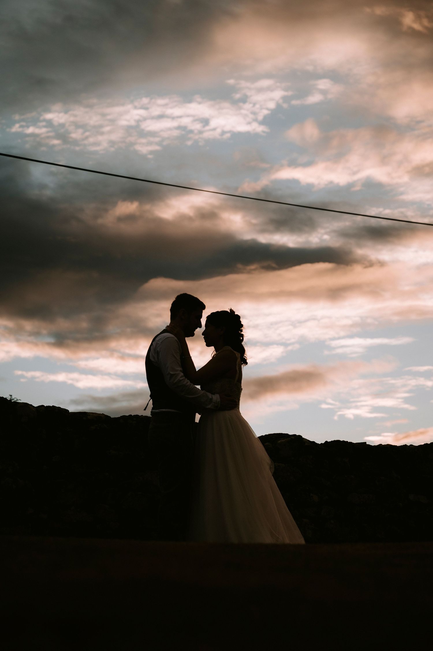 Silhouetted wedding couple against dramatic sunset sky.