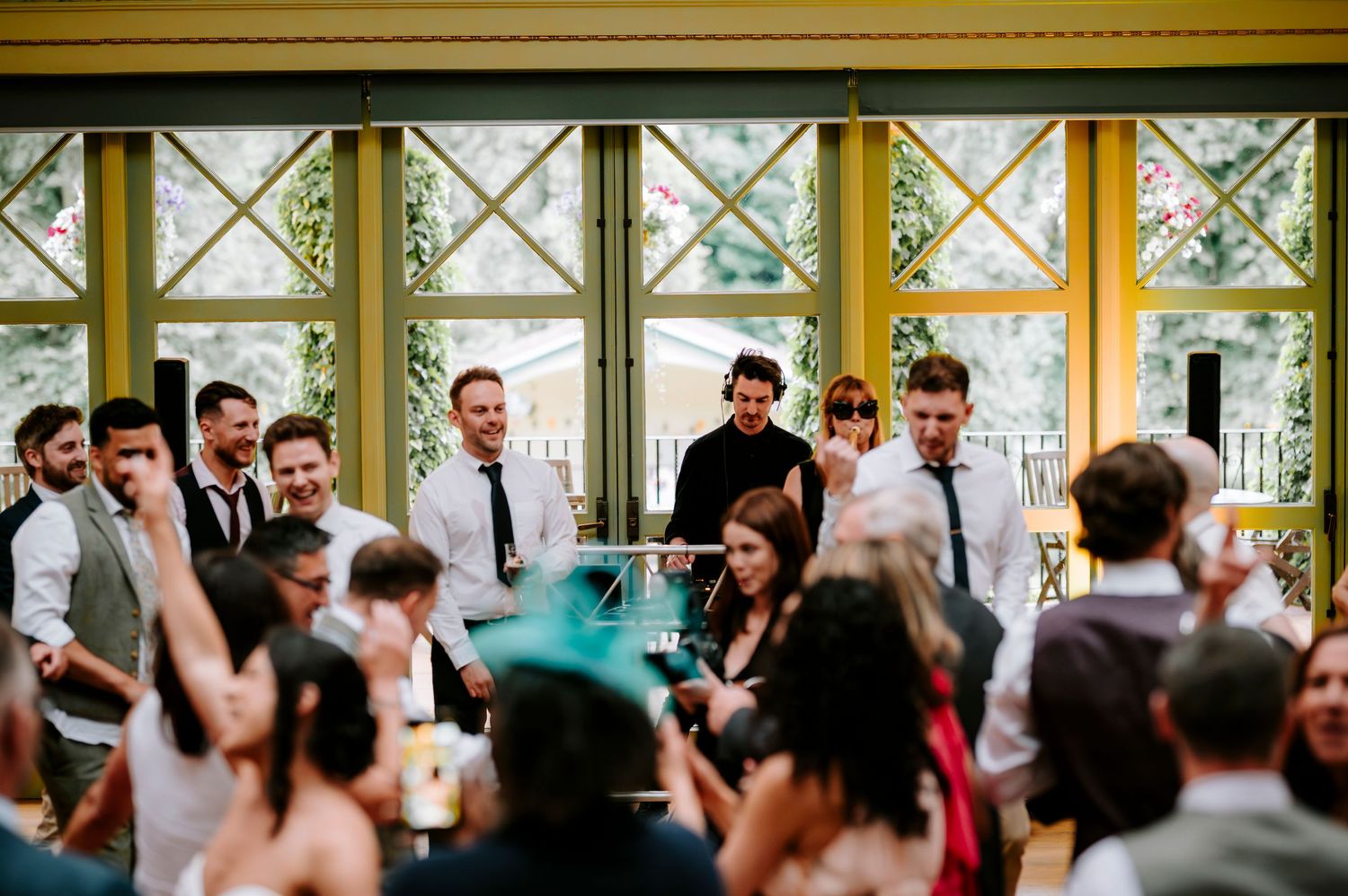 Wedding guests celebrate in front of large windows during an indoor reception.