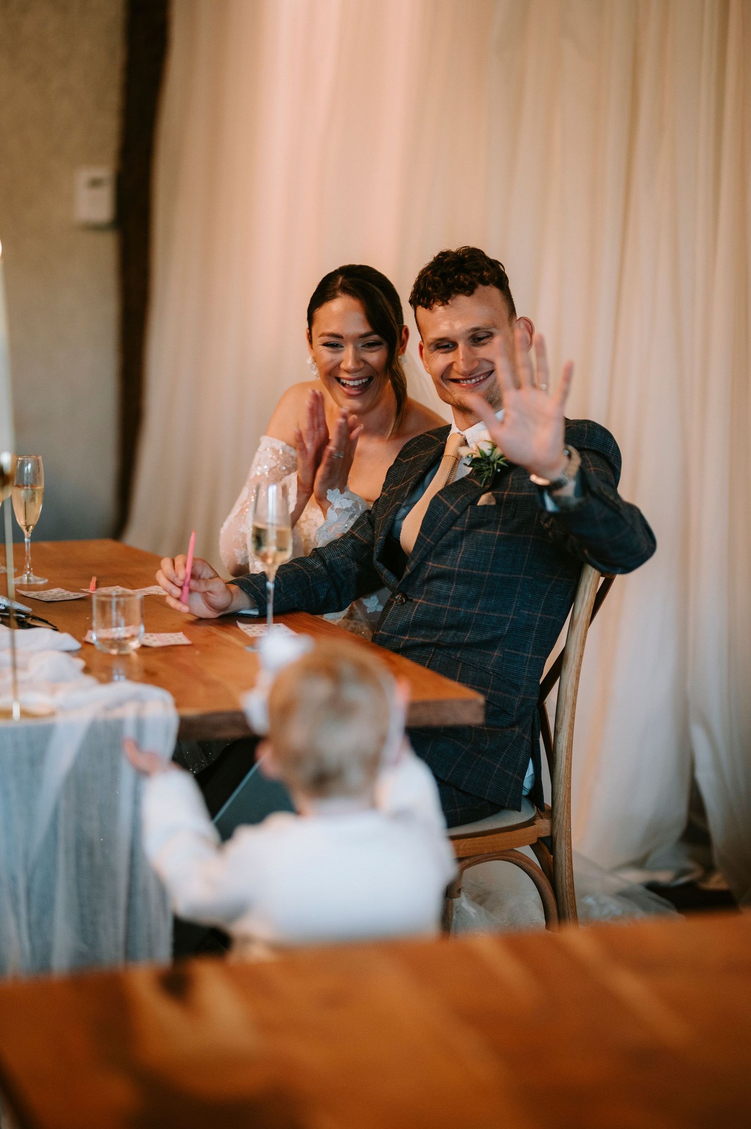 Wedding guests laugh and smile together at a reception dinner table.