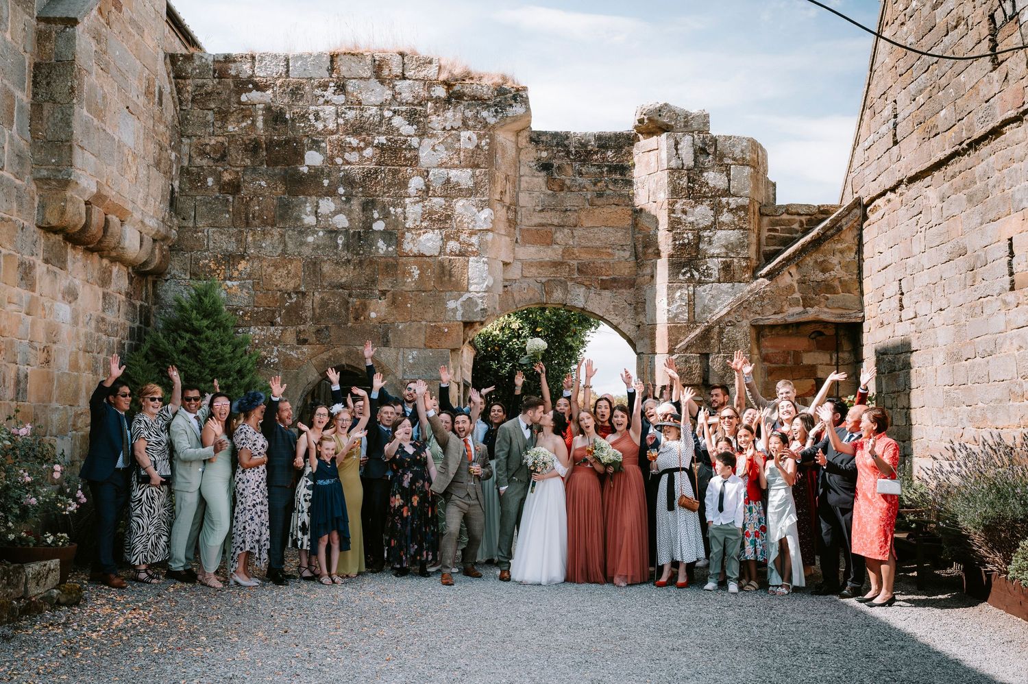 Large wedding group photo of guests gathered in front of ancient stone ruins and archway.