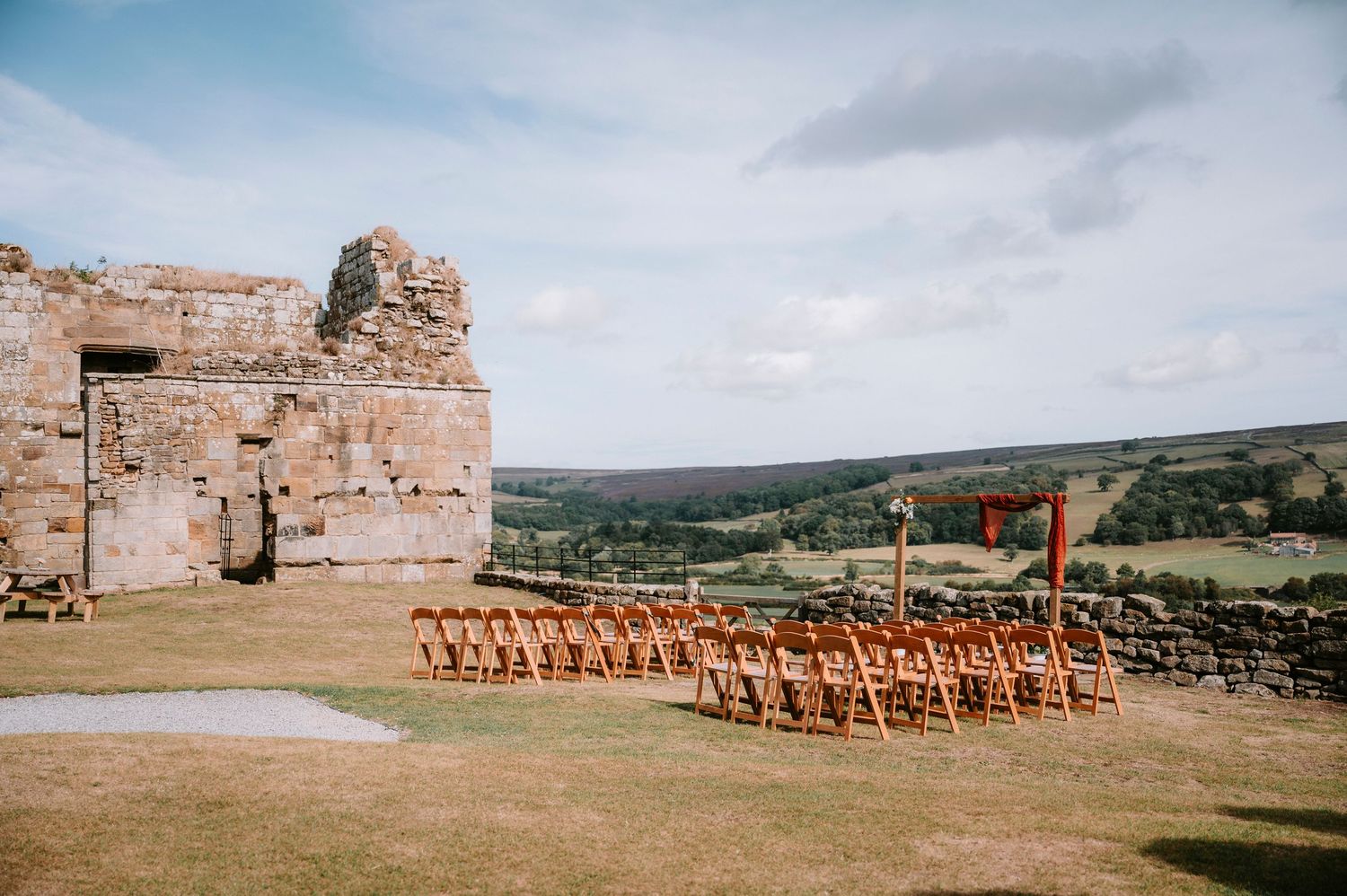 Outdoor wedding ceremony setup with wooden chairs against a scenic countryside backdrop.