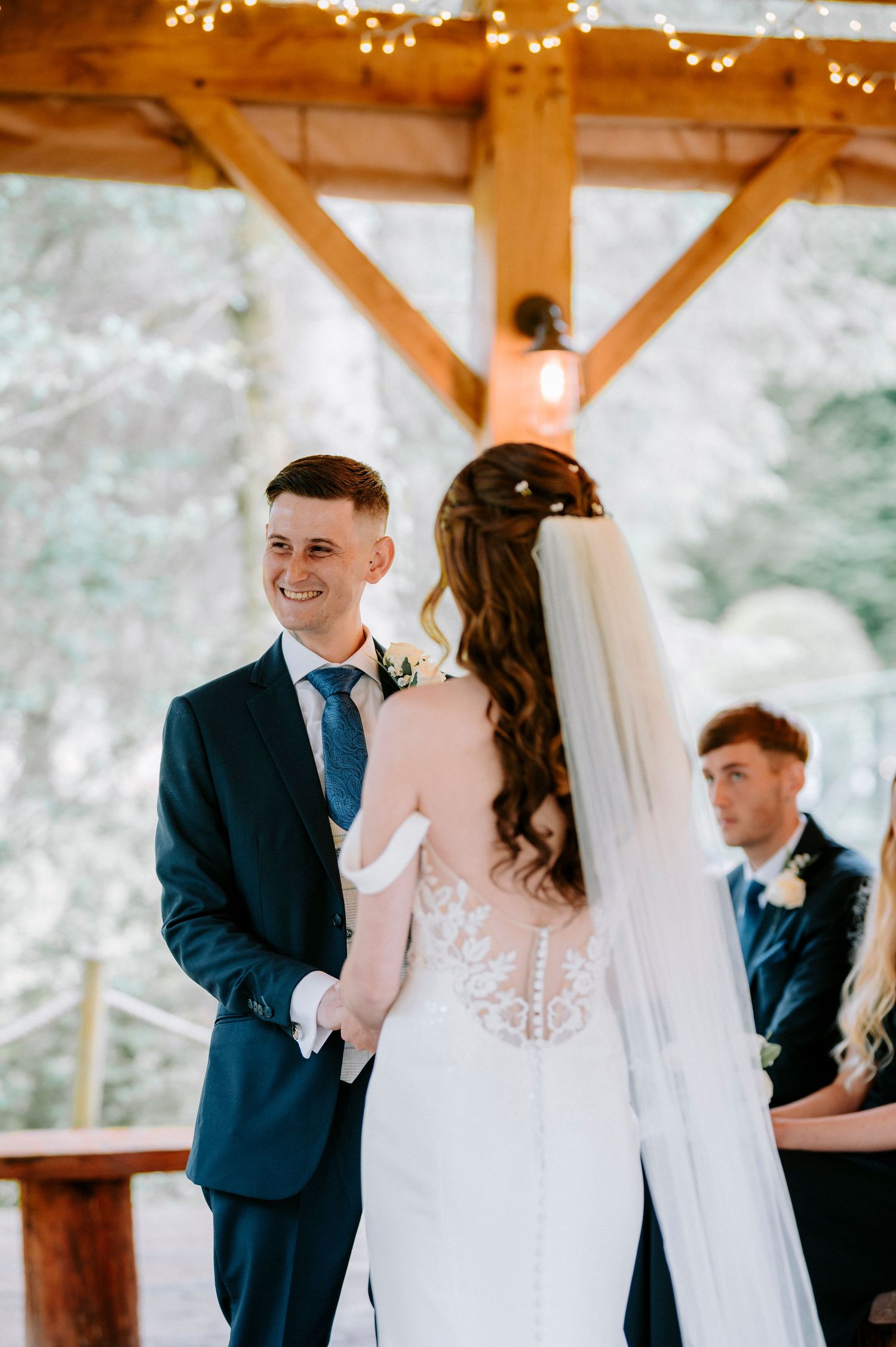 Intimate wedding ceremony moment between couple under wooden beams with twinkle lights.