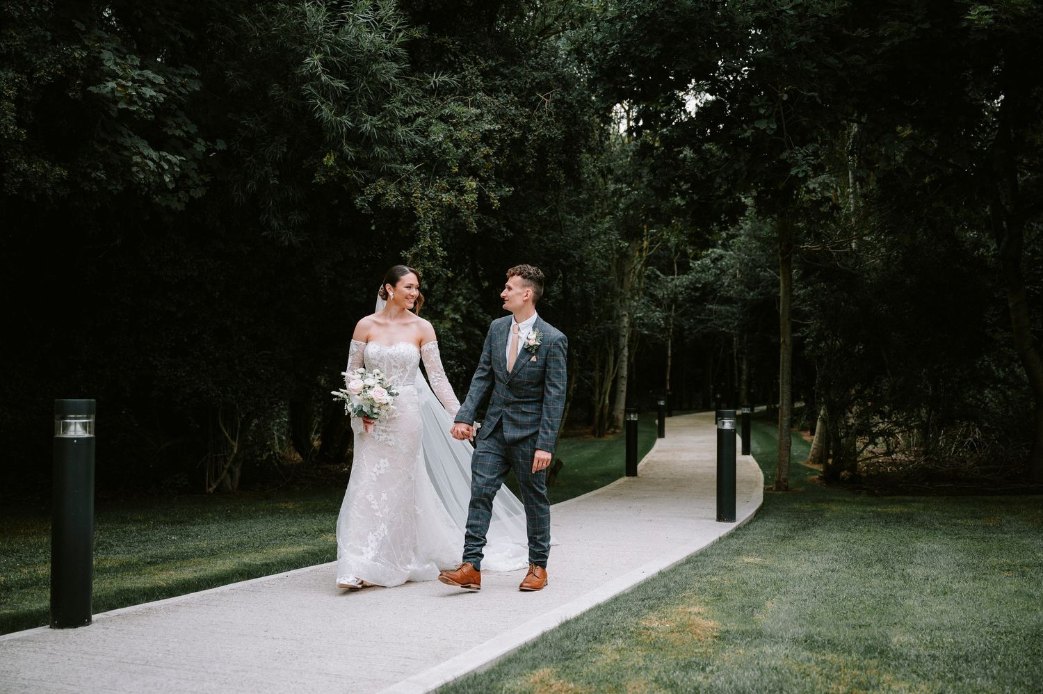 Wedding couple strolling along a tree-lined pathway during an outdoor photo session.
