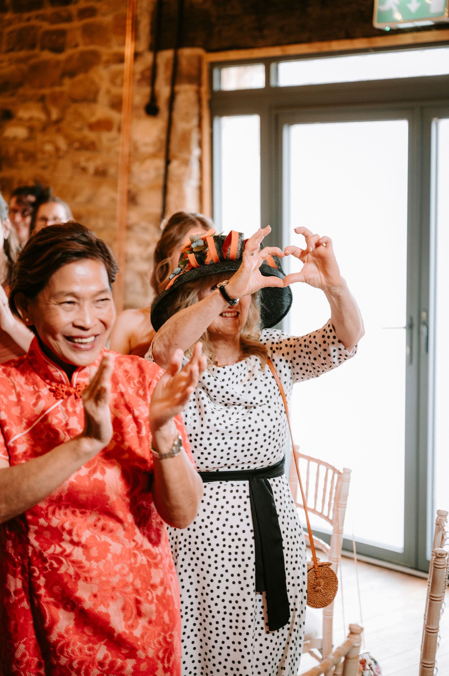 Wedding guests laugh and take photos during a joyful celebration in a rustic brick-walled venue.