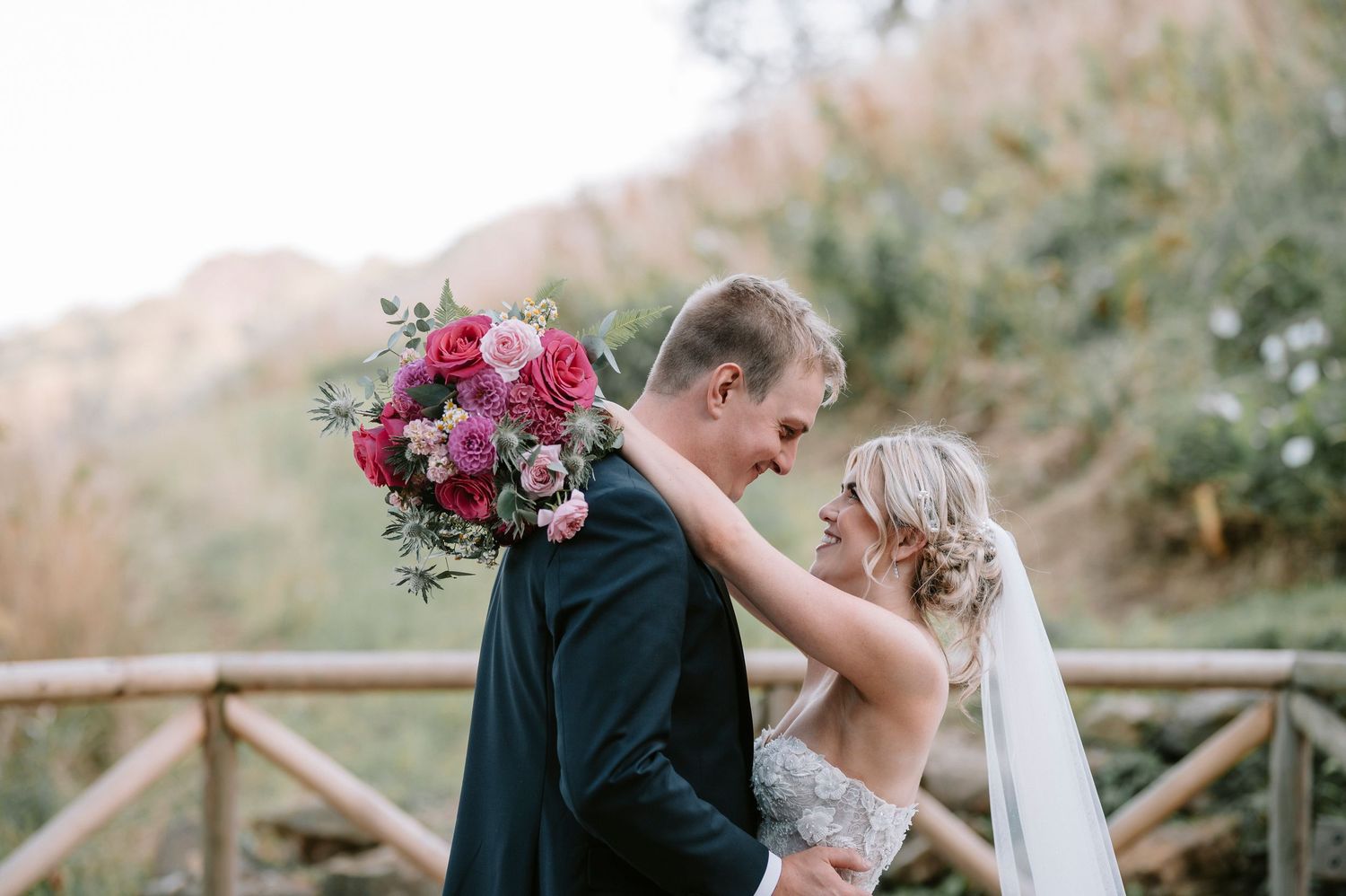 Wedding couple poses together on rustic wooden bridge surrounded by nature.