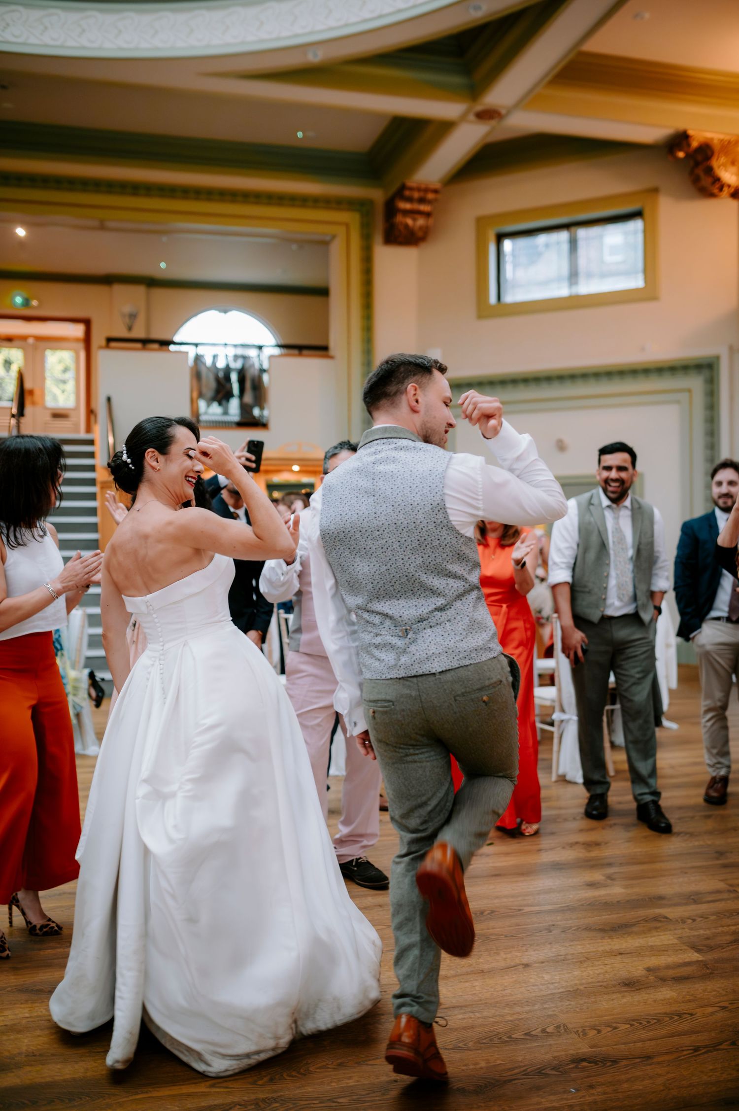 Wedding guests and couple dancing energetically at an indoor reception venue.