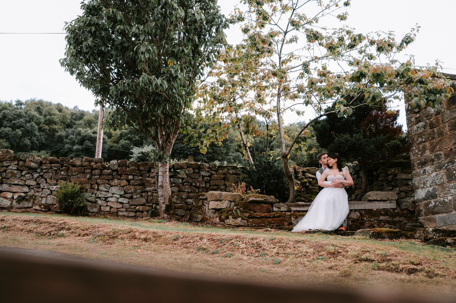 Rustic wedding photography session along a stone wall path with trees and natural scenery.