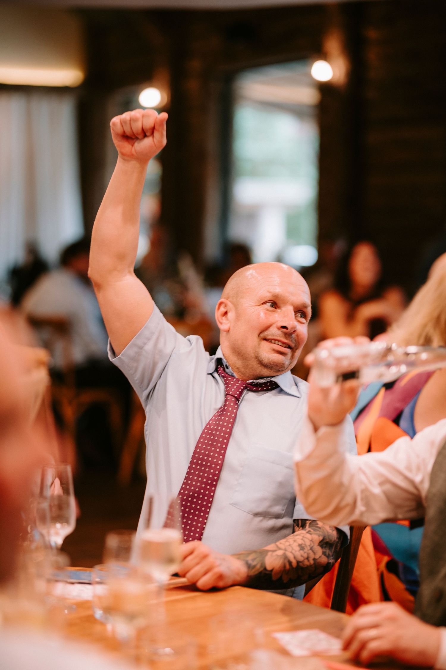 Wedding guest enthusiastically raises his fist in celebration during reception festivities.