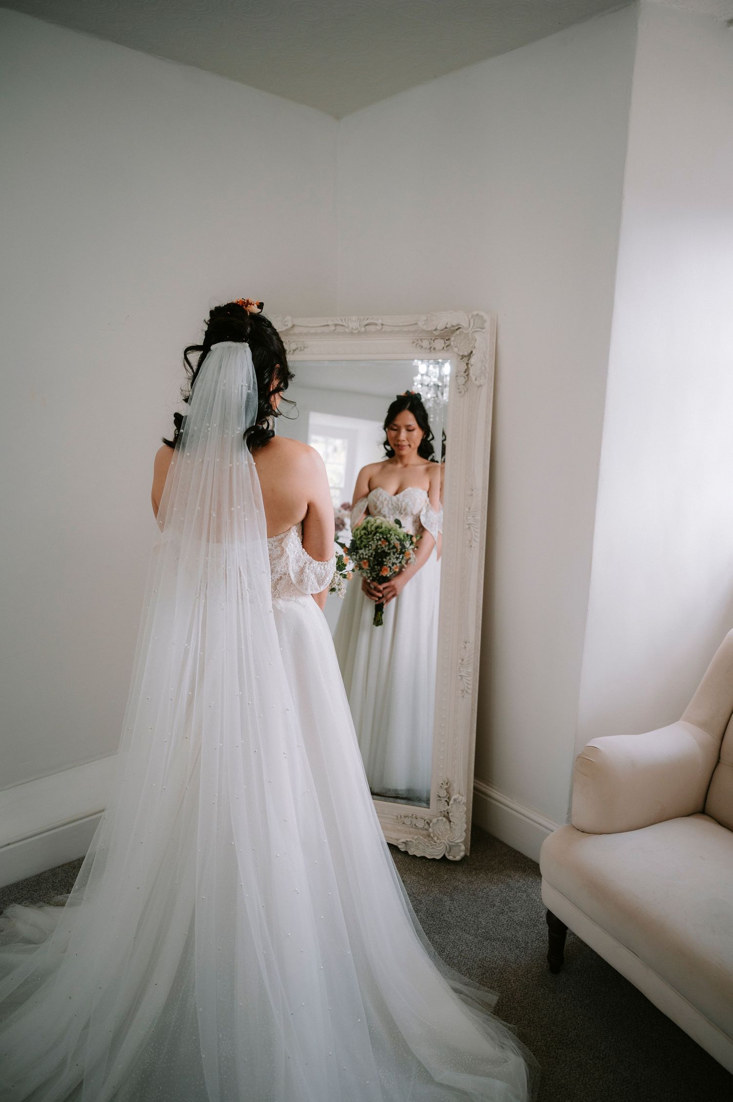 Flowing white wedding gown displayed in a bright, minimalist dressing room with mirror.