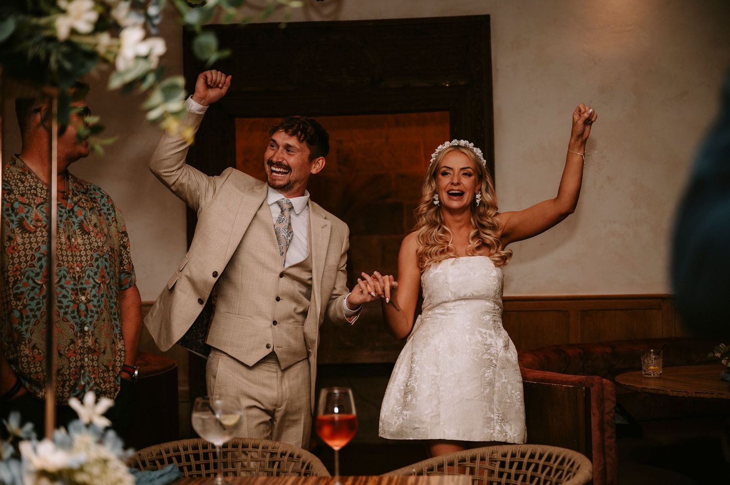 Newlyweds celebrate with raised arms during wedding reception in rustic indoor venue.
