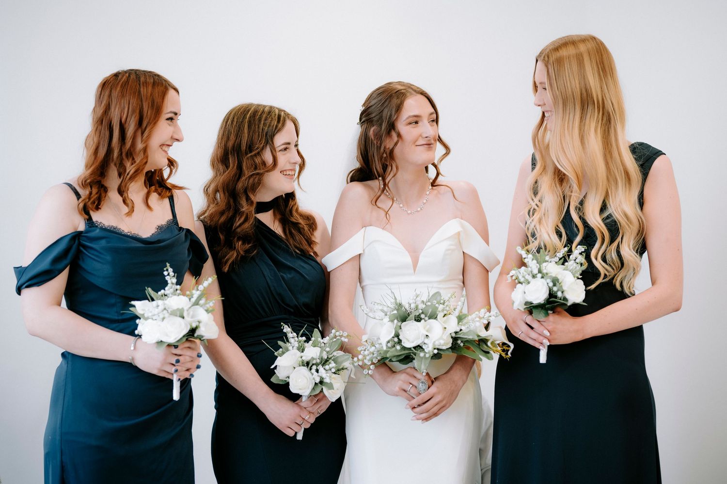 Bridesmaids in navy dresses holding white bouquets against white background.
