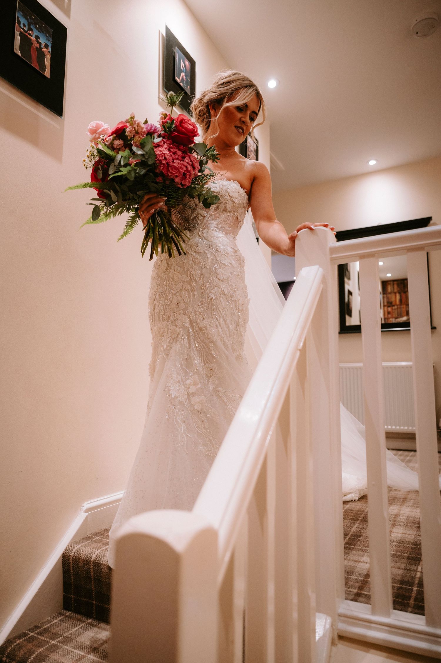 Elegant bridal silhouette ascending stairs with flowing veil and pink bouquet.