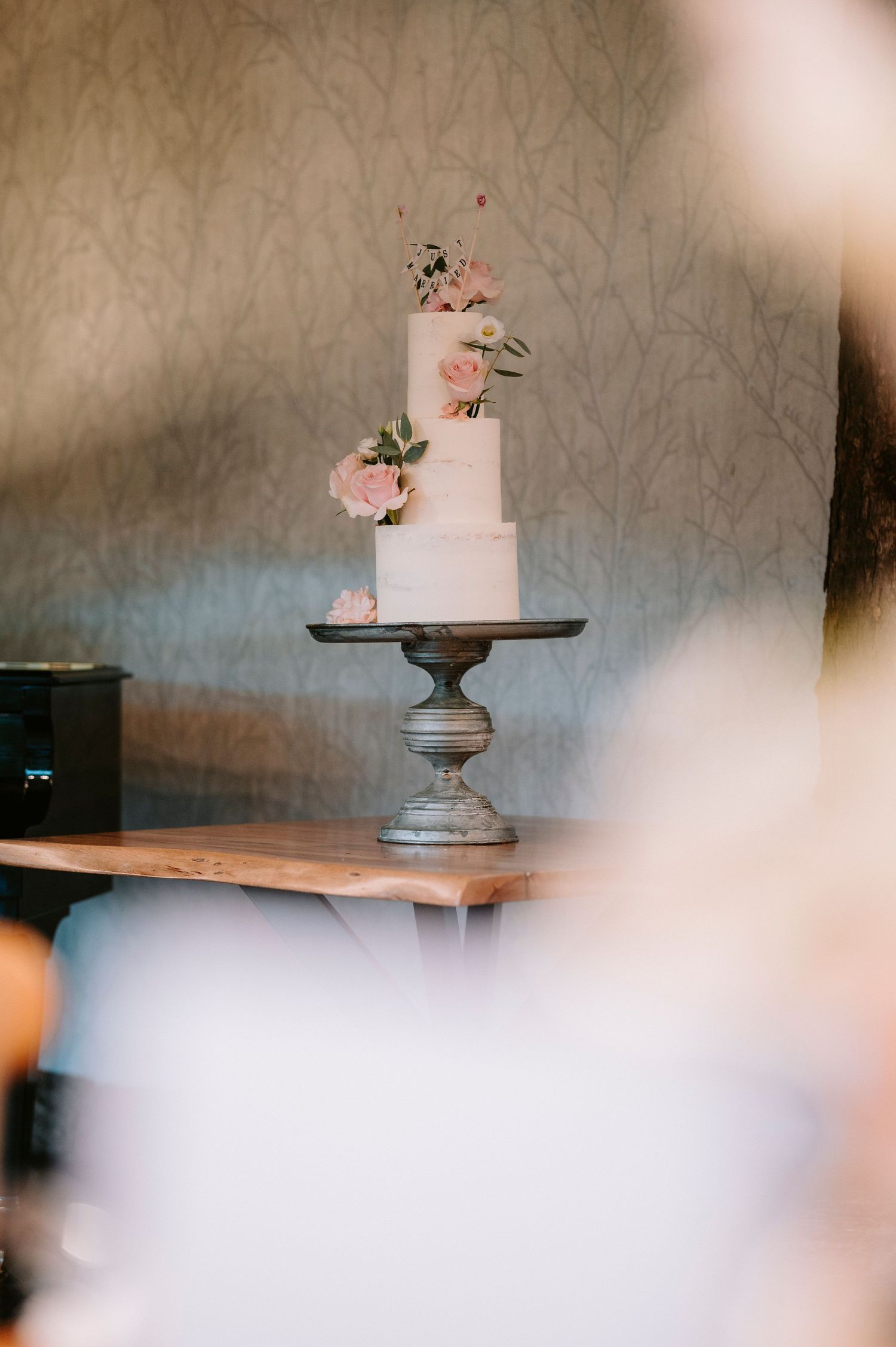 Elegant white wedding cake with pink floral decorations displayed on an ornate silver pedestal stand.