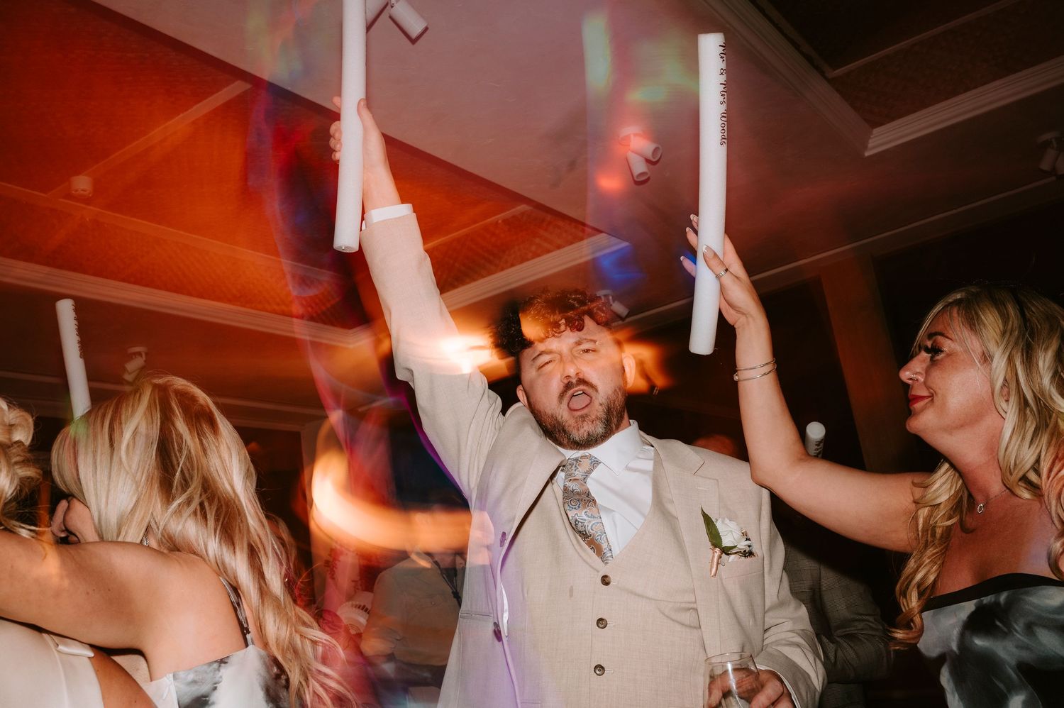 Wedding celebration with enthusiastic dancing and raised arms under red party lights.