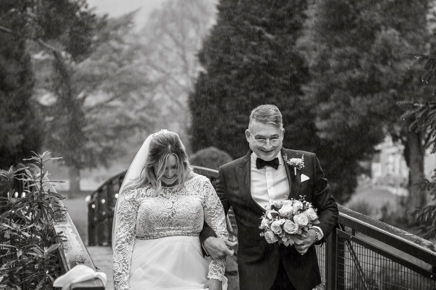 A black and white photo capturing a joyful wedding moment on a wooden walkway.