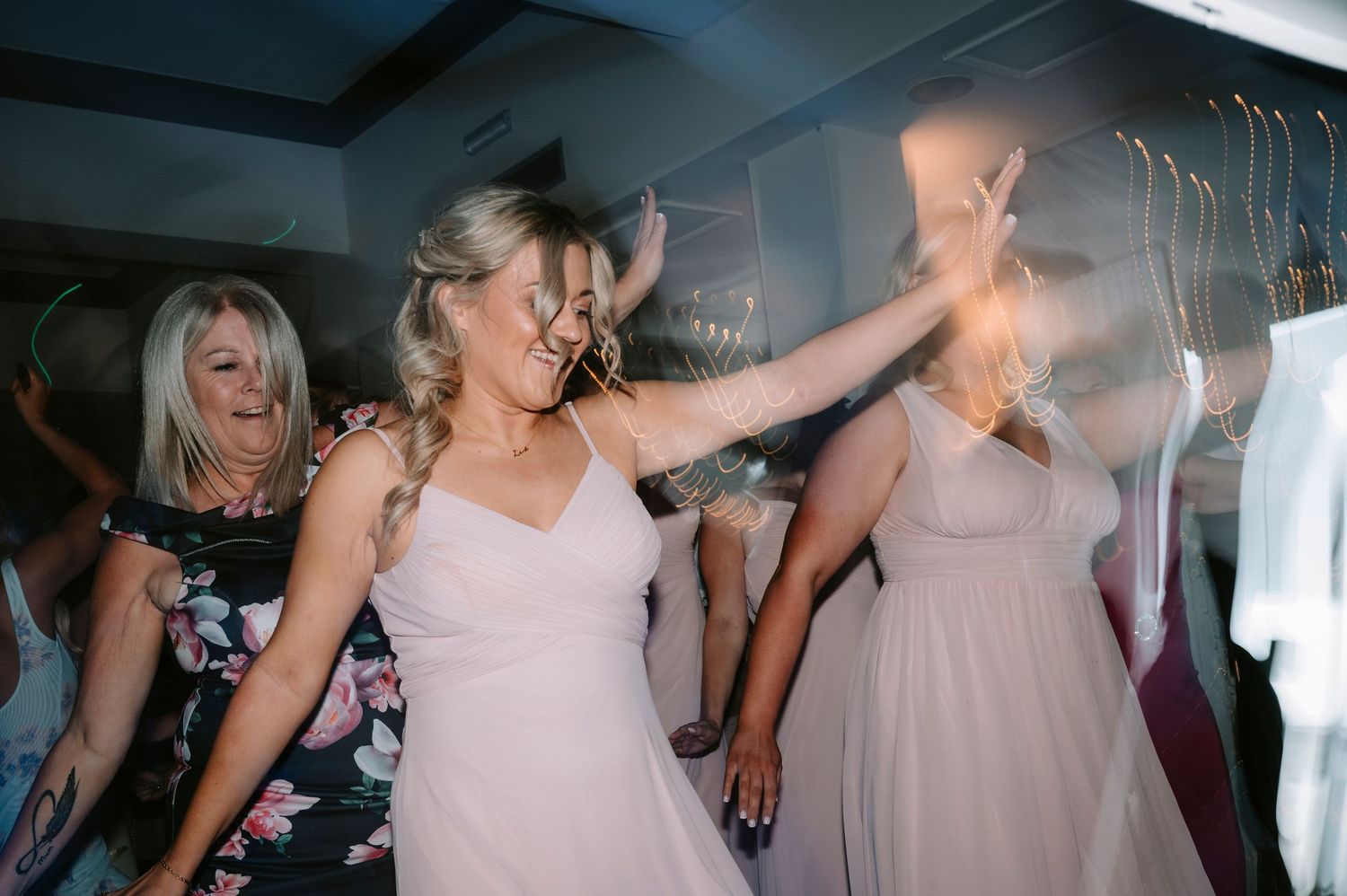 Bridesmaids in pink dresses dance together during wedding reception celebrations.