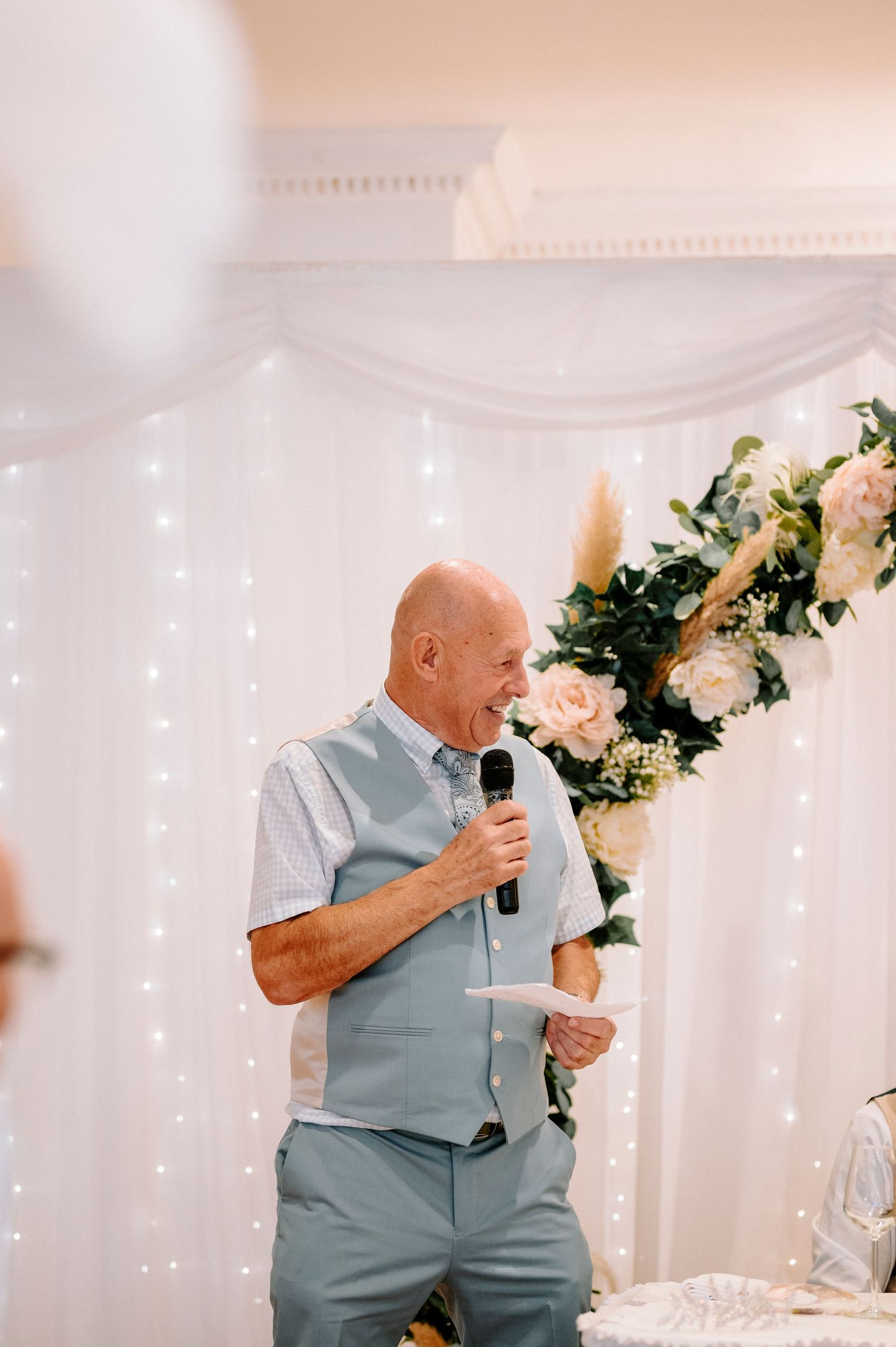 Wedding reception speech being given against a backdrop of twinkling fairy lights and floral arrangements.