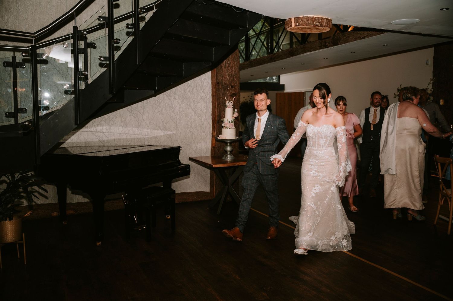 A couple dances together in an elegant venue with dark wooden staircase and ambient lighting.