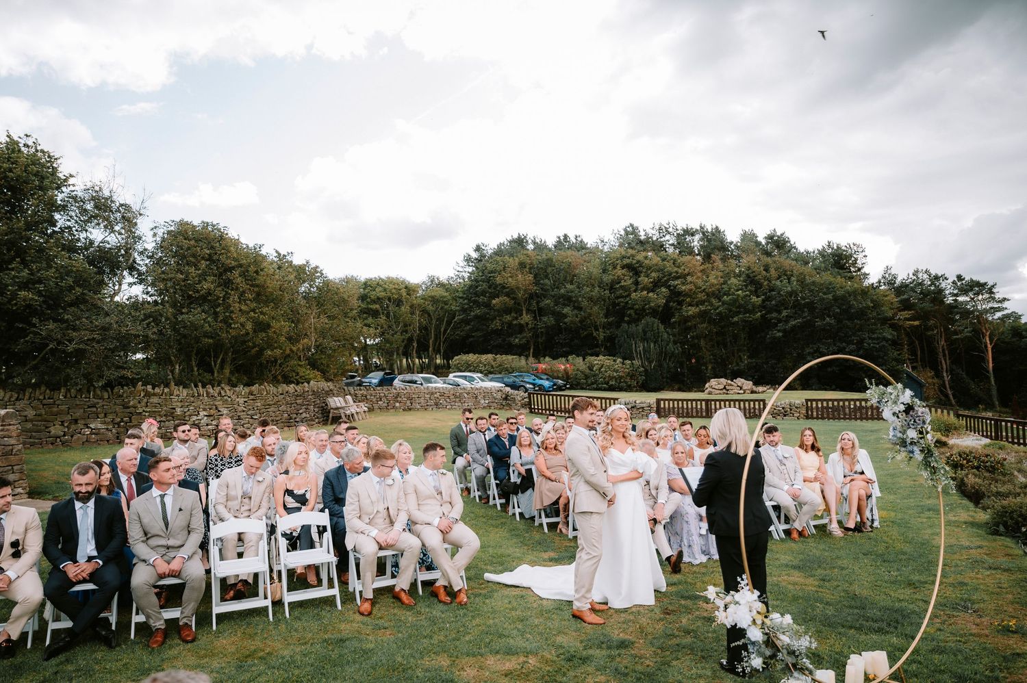 Outdoor wedding ceremony with white chairs and floral arch set against a backdrop of rolling hills and trees.