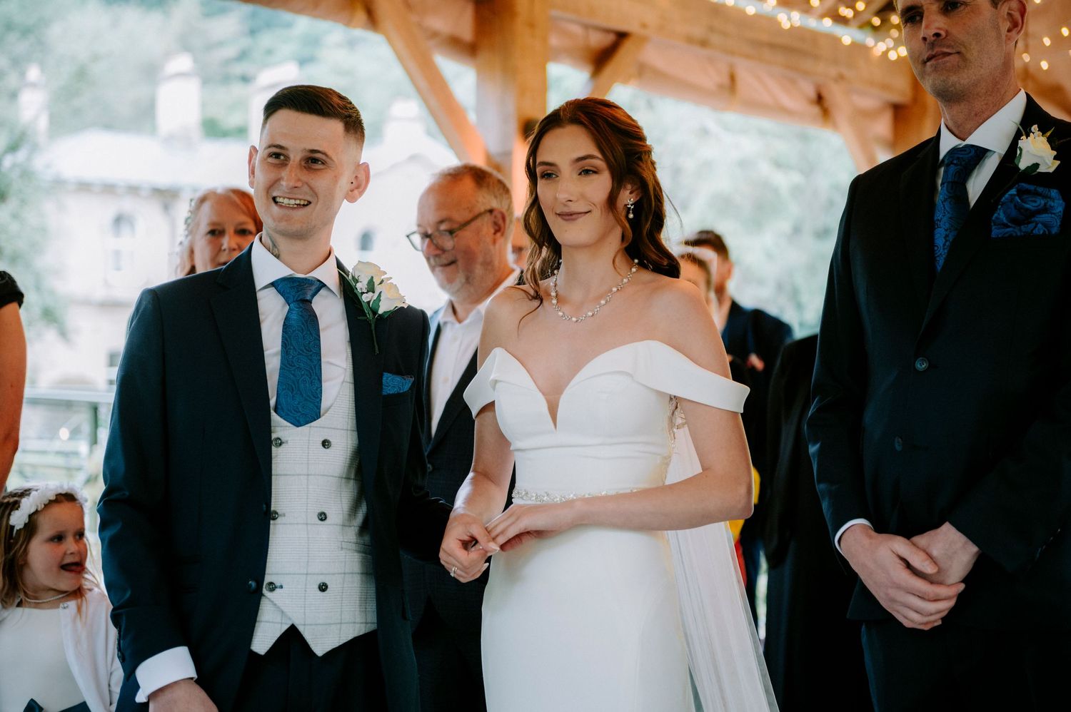 Indoor wedding ceremony with guests seated under string lights and wooden beams.
