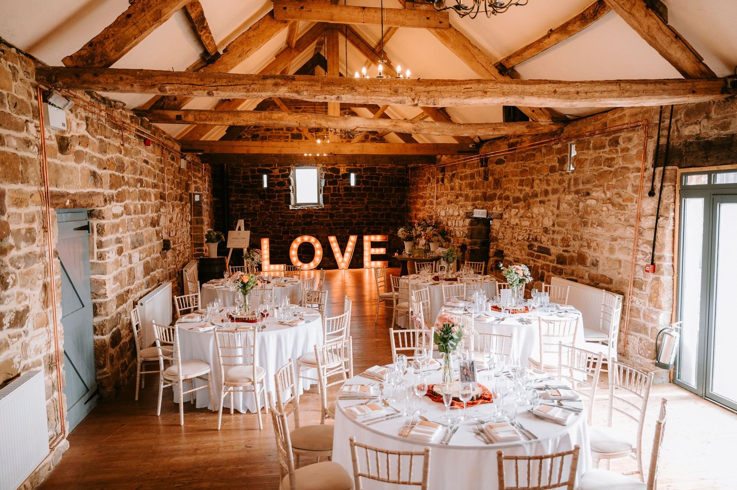Rustic wedding reception venue with exposed beams, stone walls and illuminated LOVE sign.