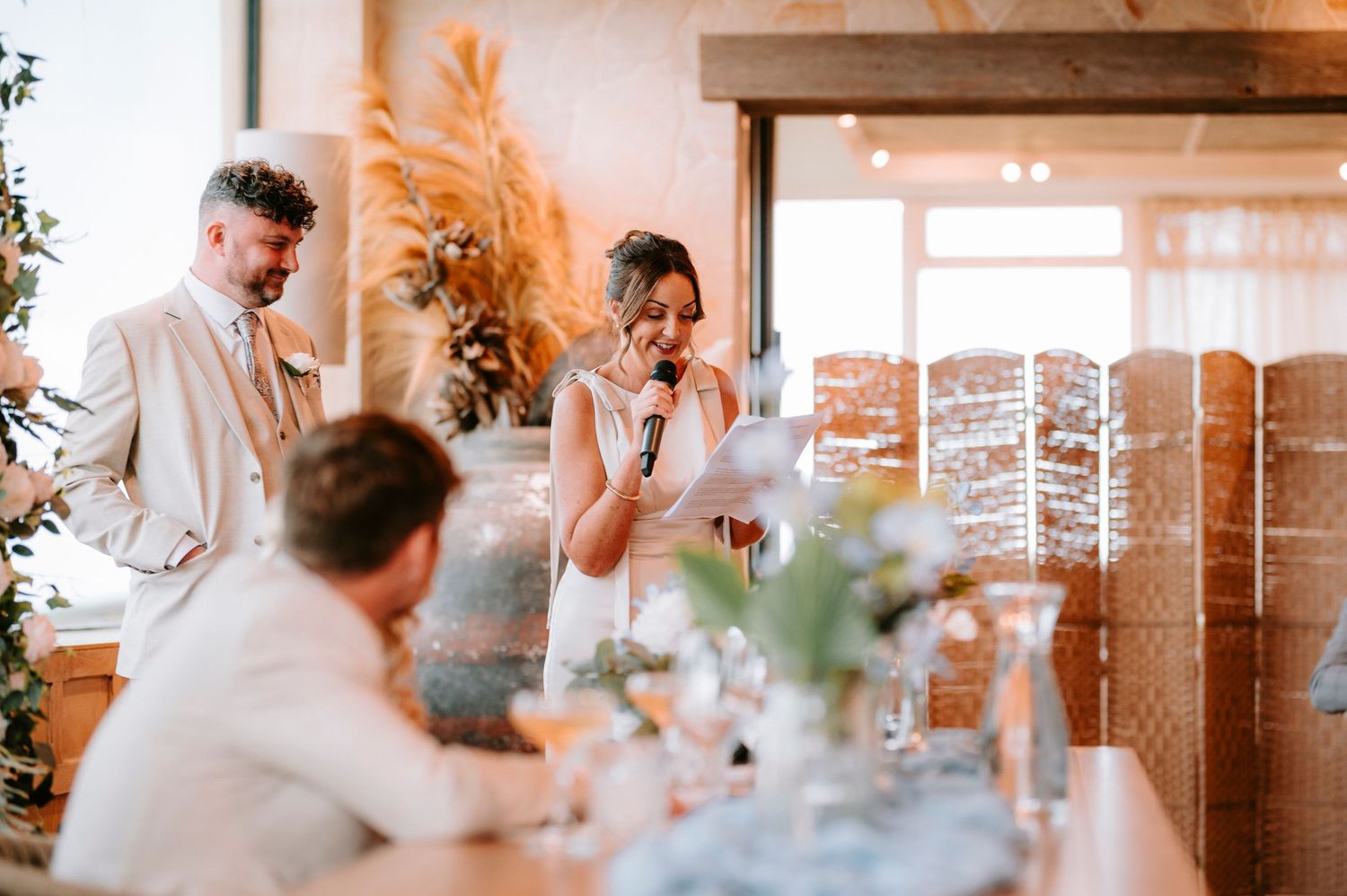 Wedding reception speech moment with elegant table settings and pampas grass decor.