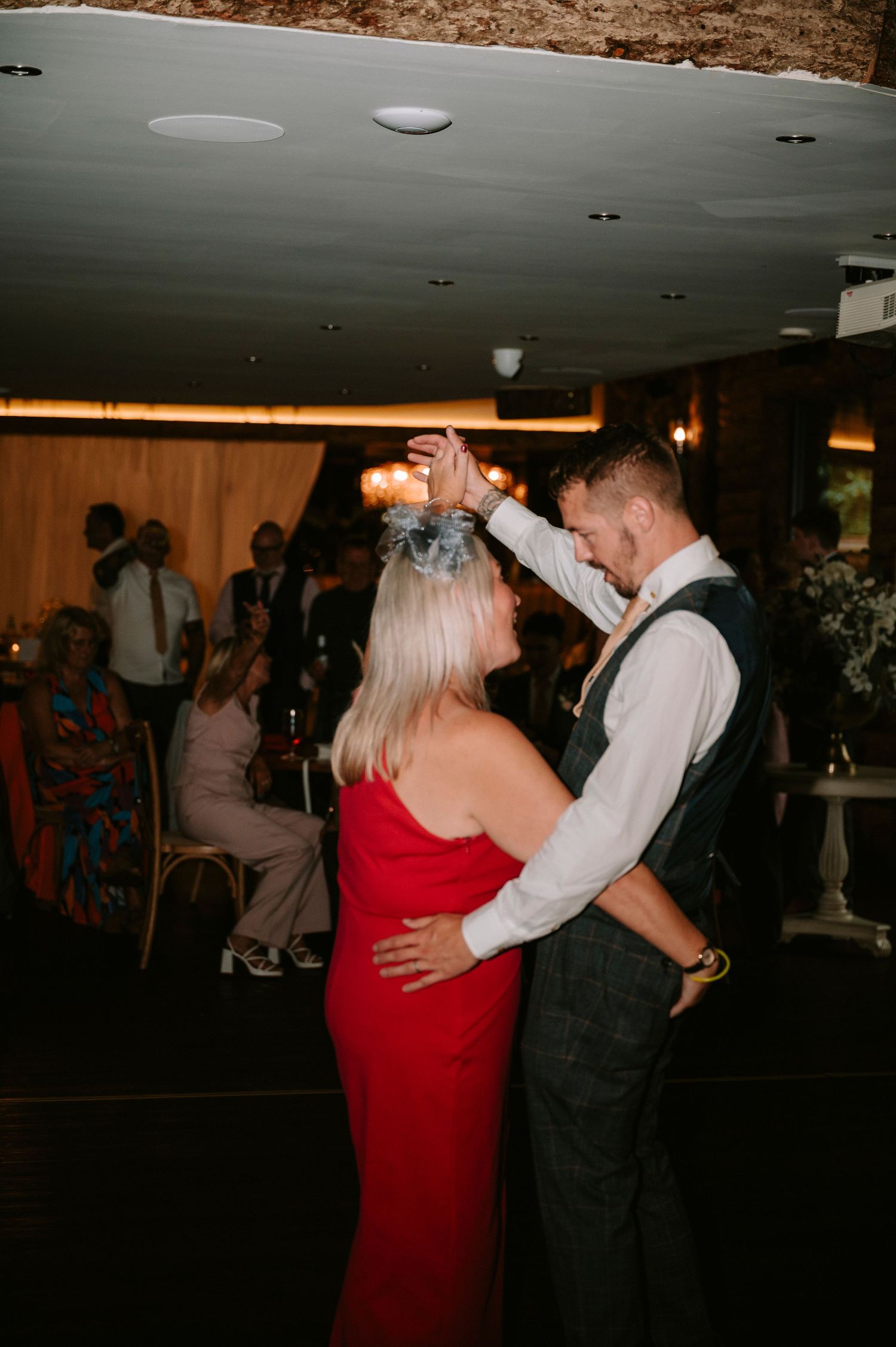 Couple dancing together at wedding reception, woman in red dress and man in formal vest.