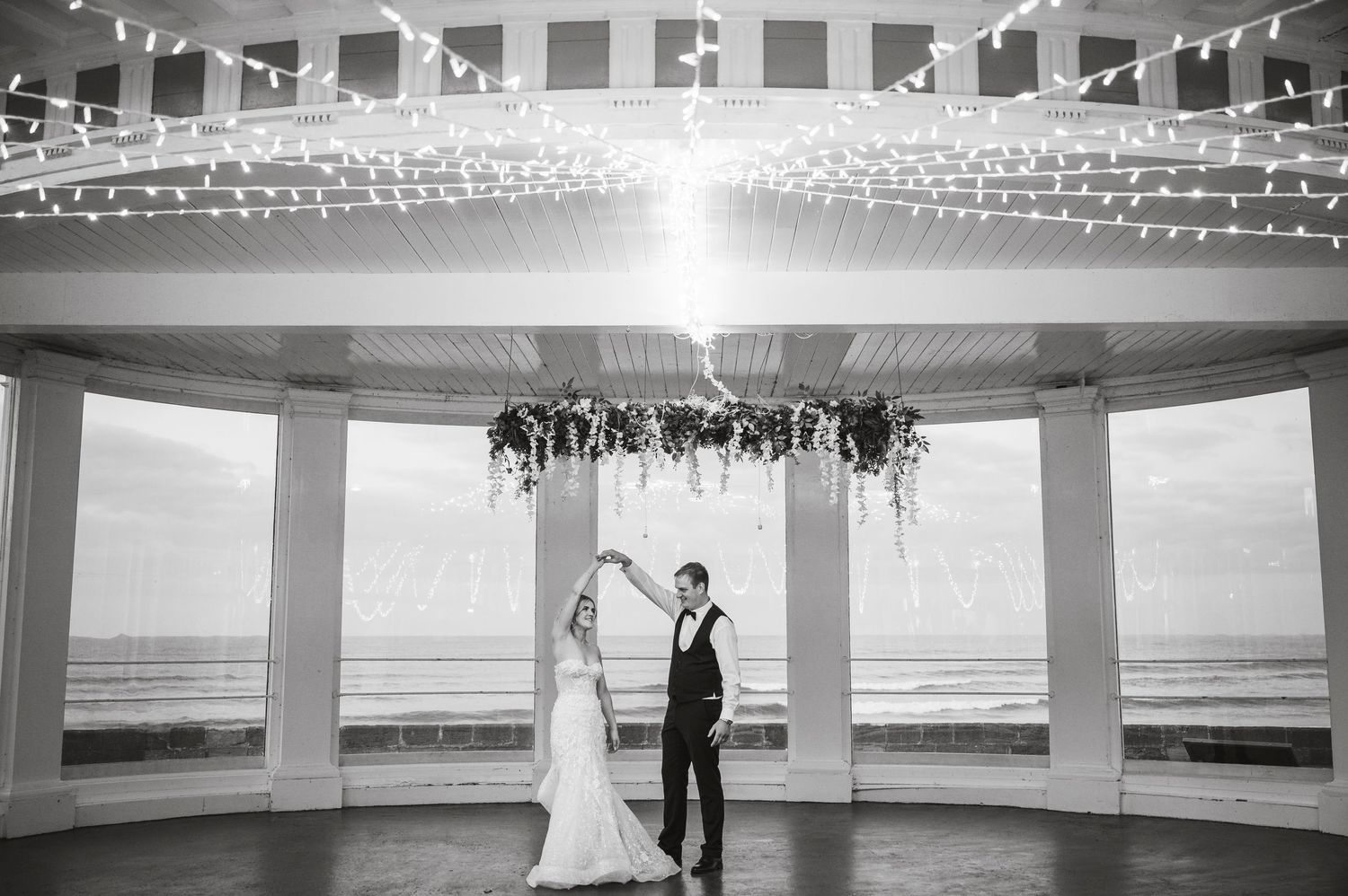 Black and white panoramic view of an elegant wedding venue with string lights and columns.