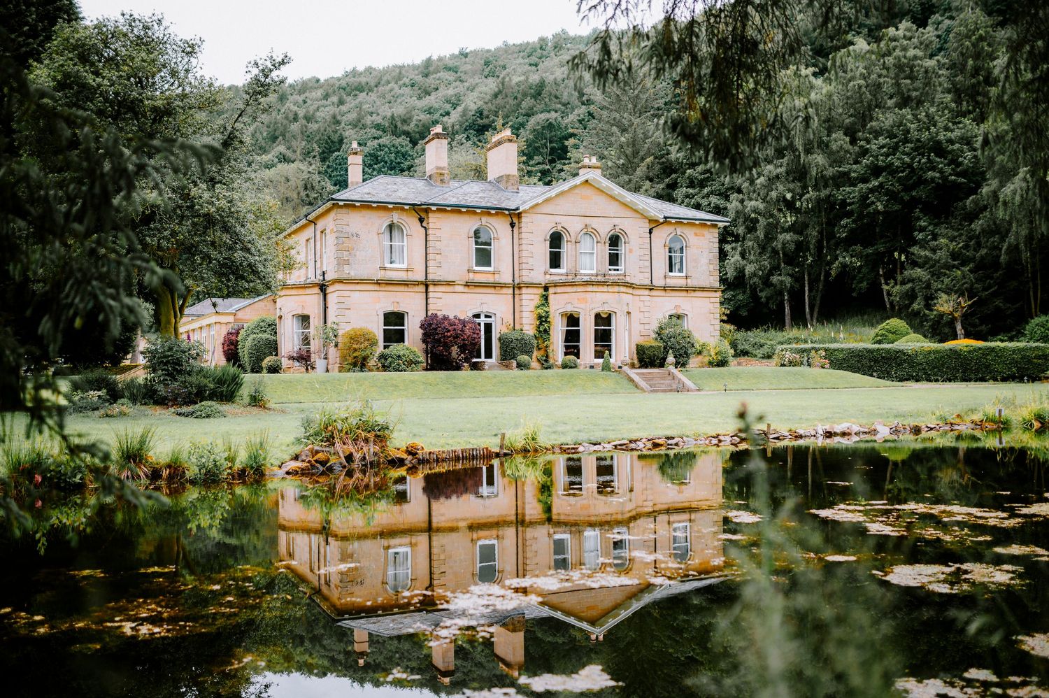 Elegant country estate venue with reflective pond and manicured grounds on a cloudy day.