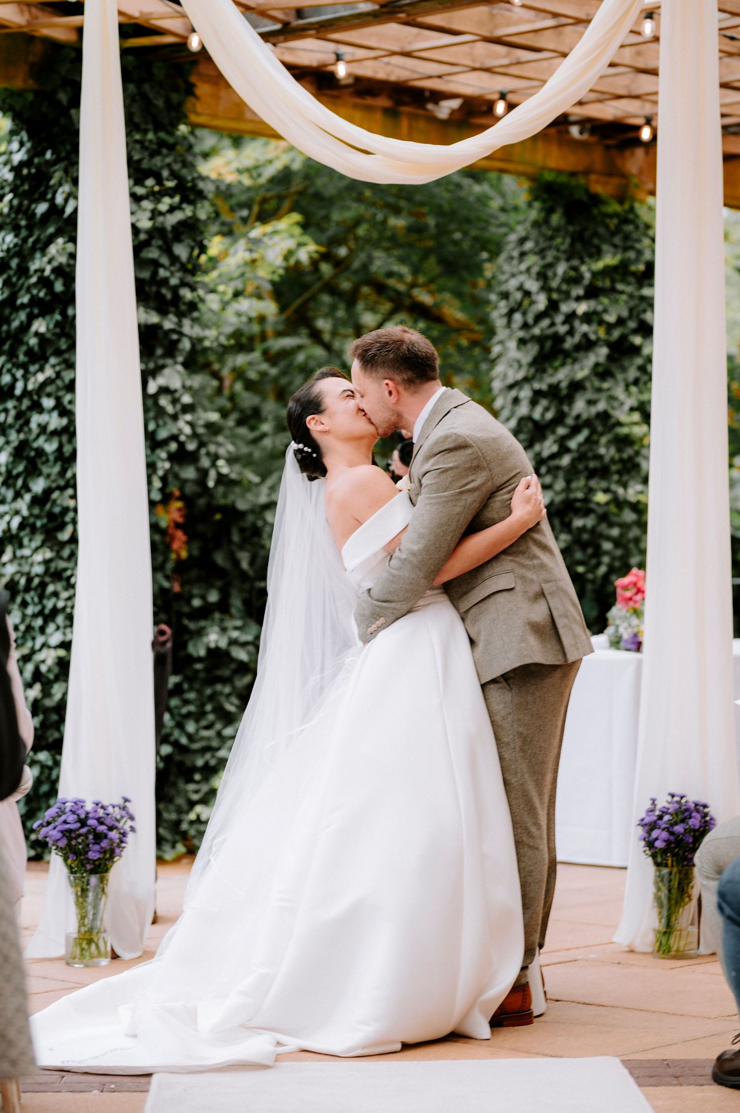 Romantic dip kiss between newlyweds on outdoor wedding stage.
