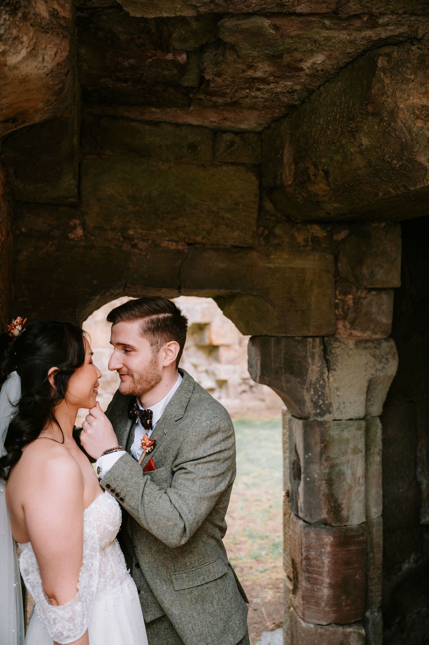 Intimate wedding moment captured under rustic stone archway.