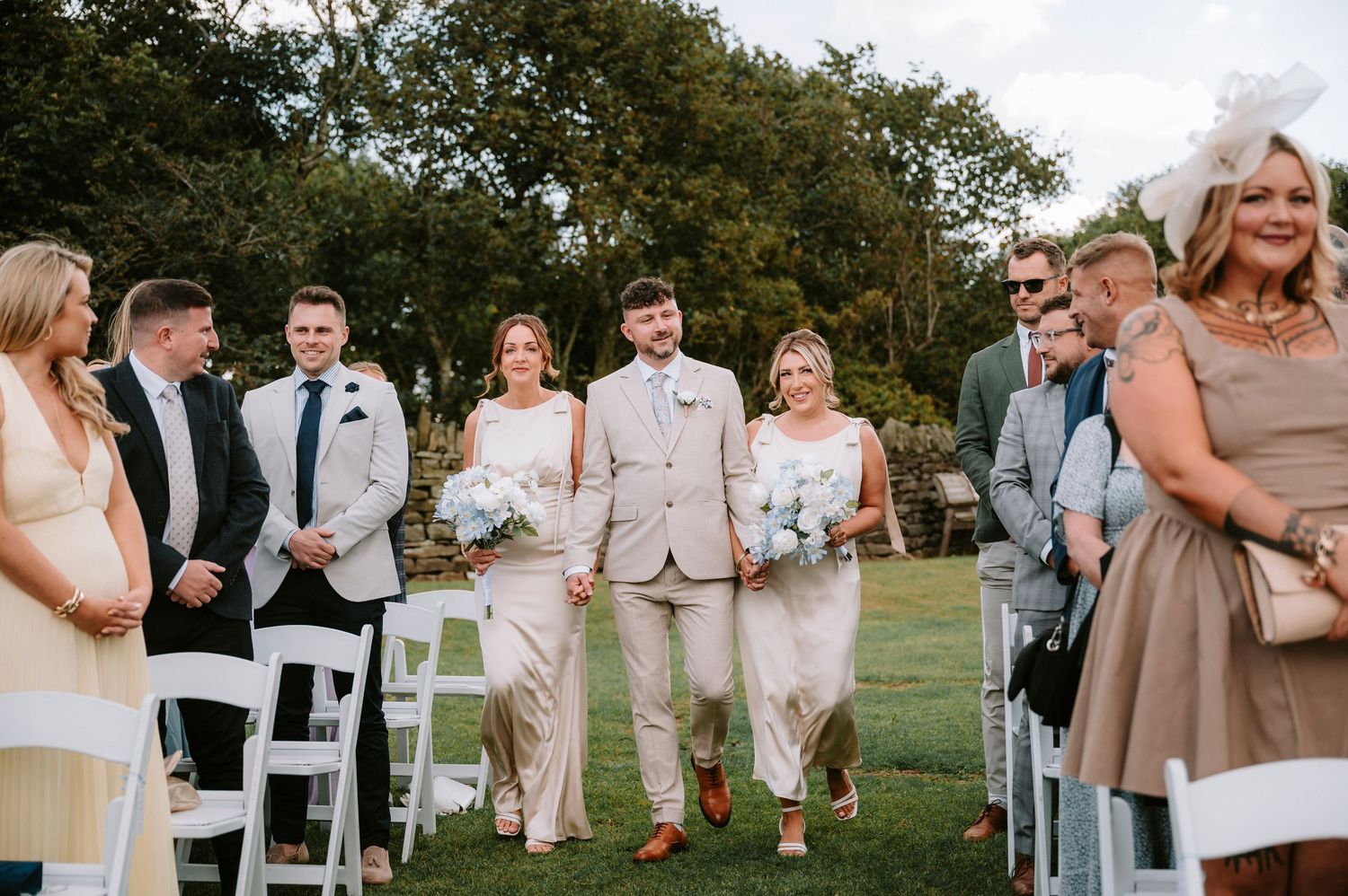 Wedding party members in beige and neutral attire gather outdoors for candid group photos.
