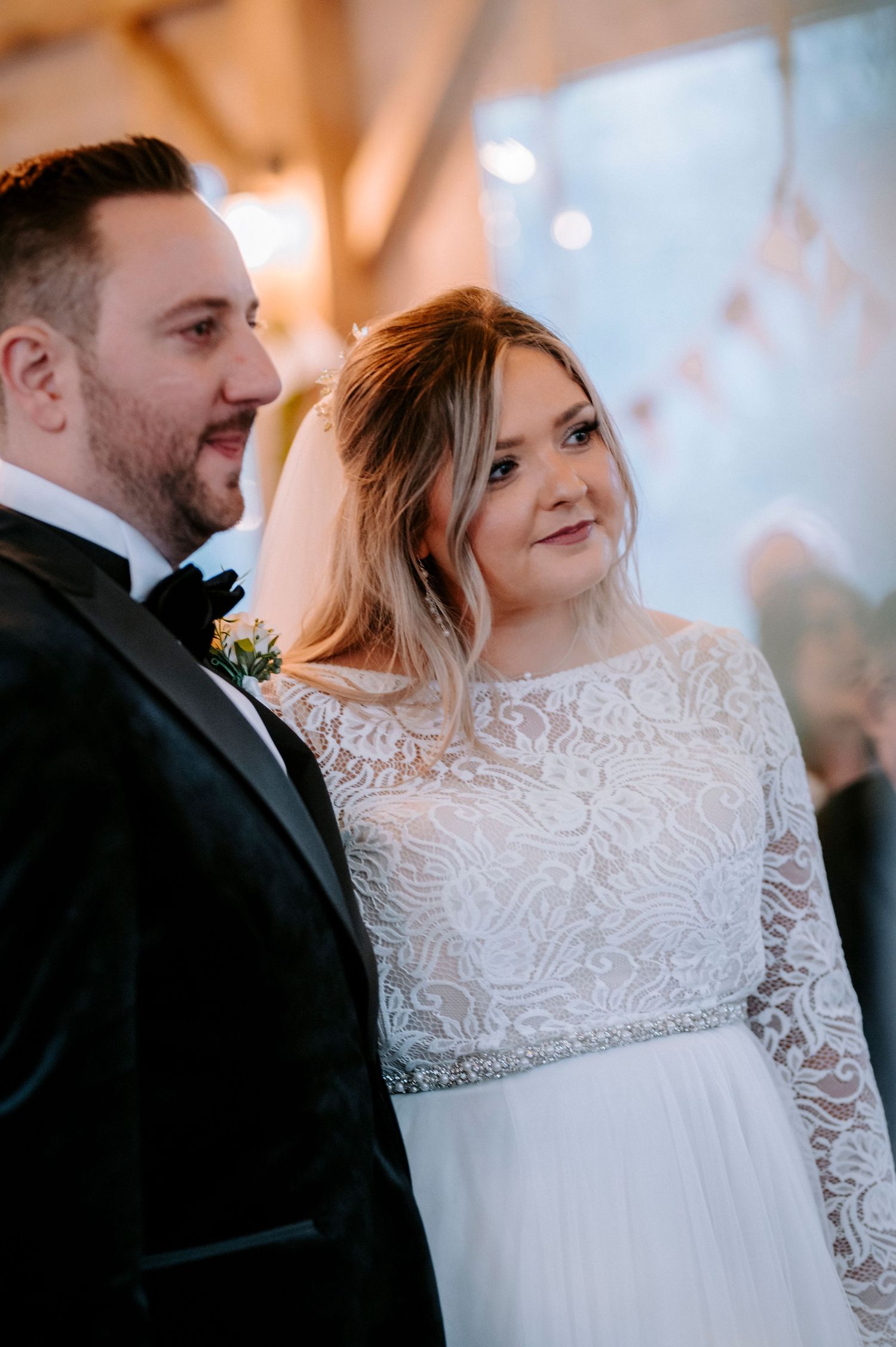 Close-up wedding portrait showing intricate lace details of a white bridal gown against warm lighting.