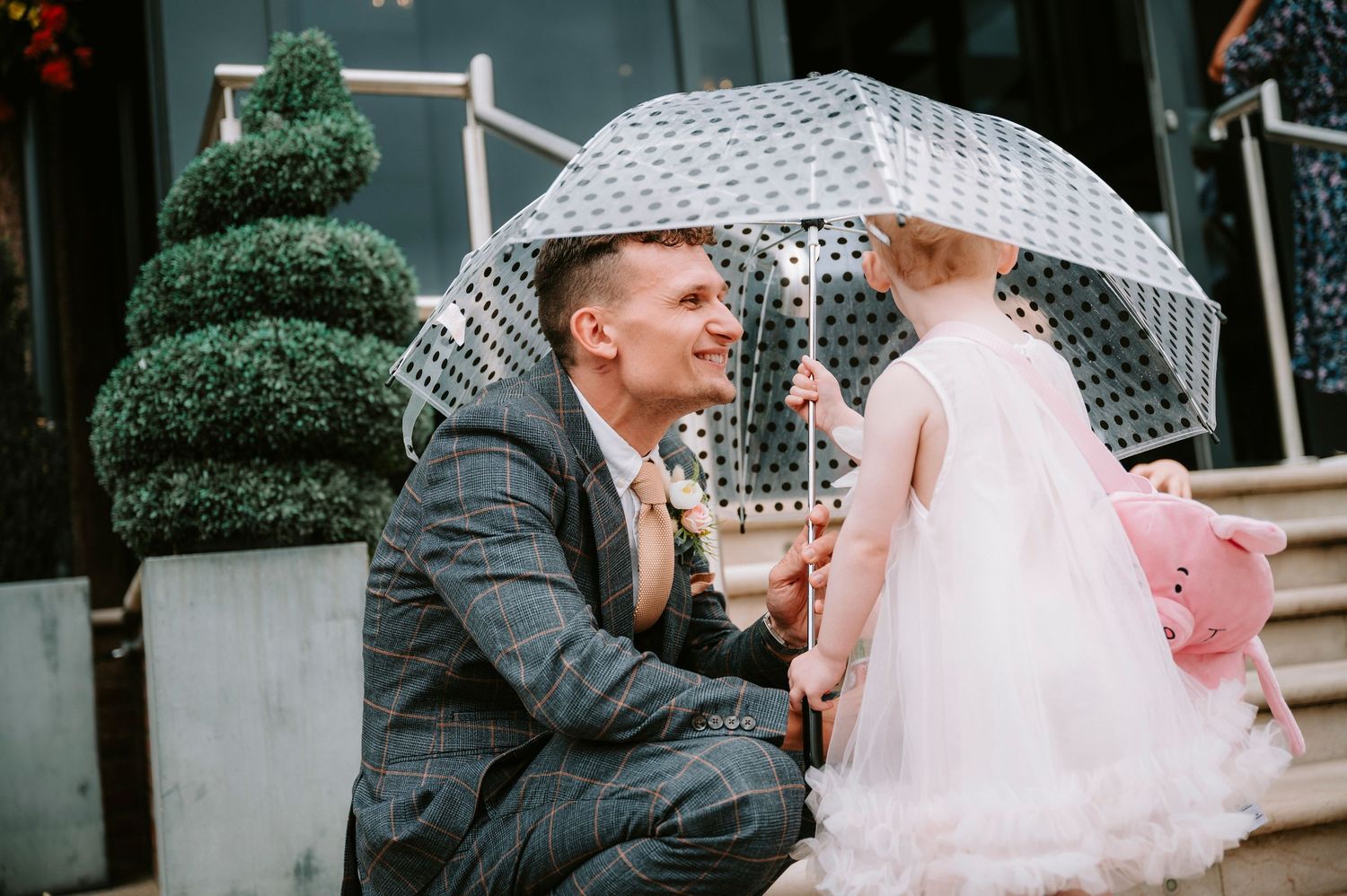 Couple shares a romantic moment under a white umbrella outside their wedding venue.