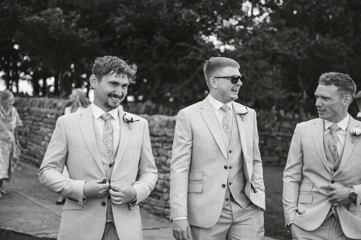 Groomsmen in light beige suits standing together outdoors at a formal event.