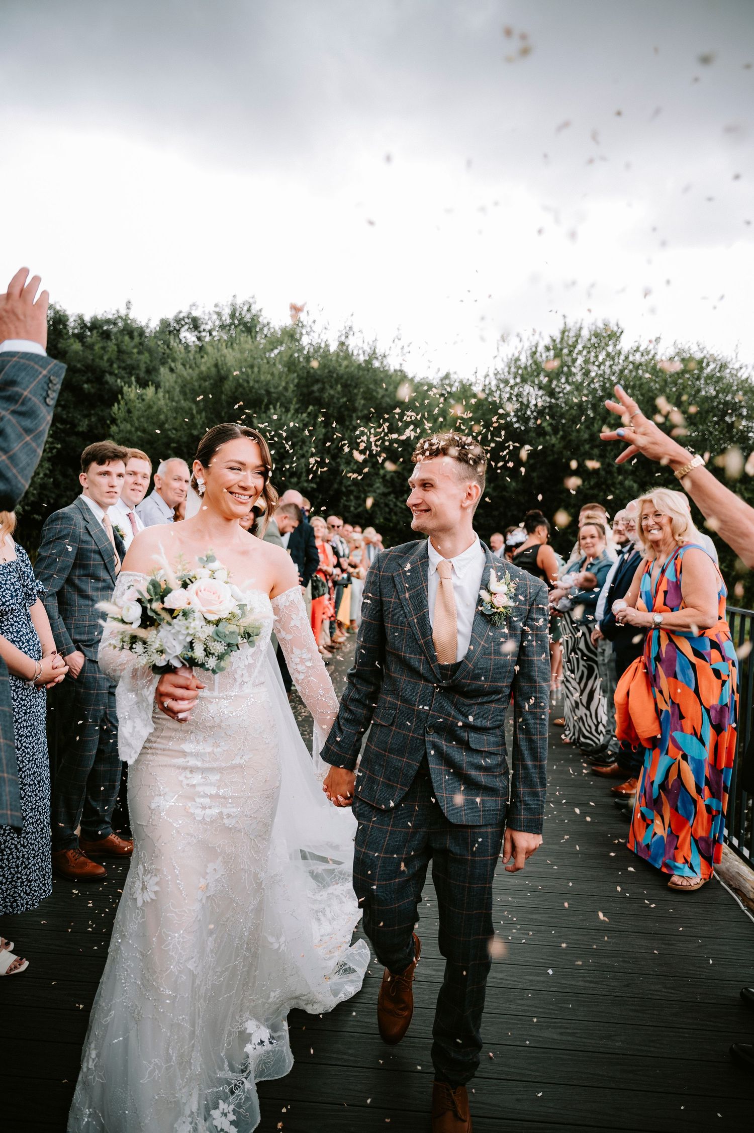 Wedding guests celebrate with confetti during an outdoor daytime celebration.