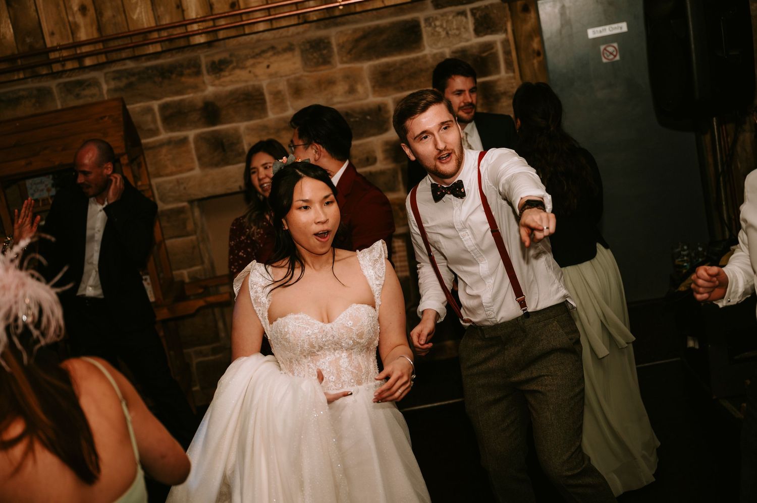 Wedding party celebrates in a dimly lit rustic venue with exposed brick walls.