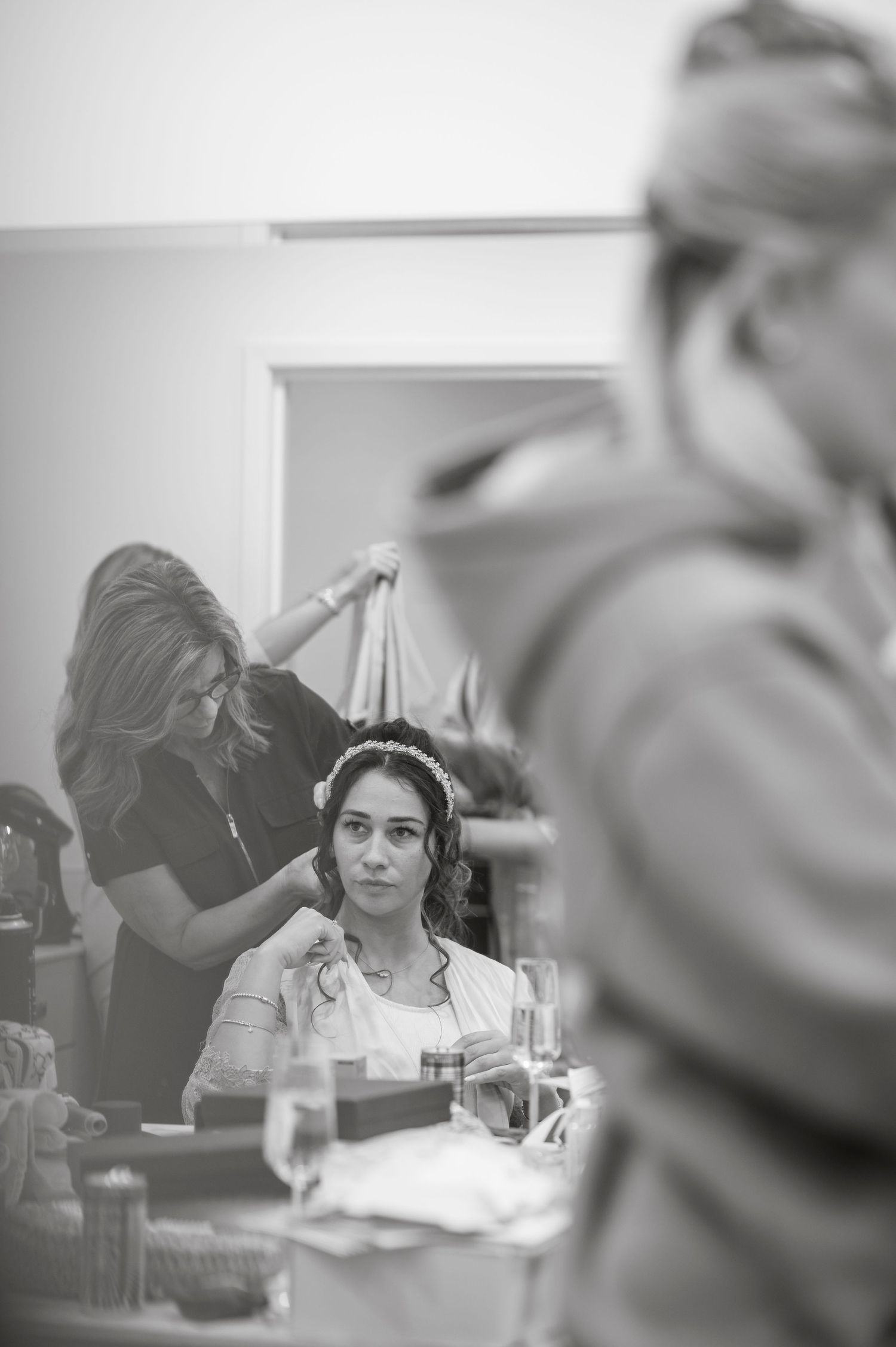 Black and white image showing preparations in a bridal suite with soft window lighting.