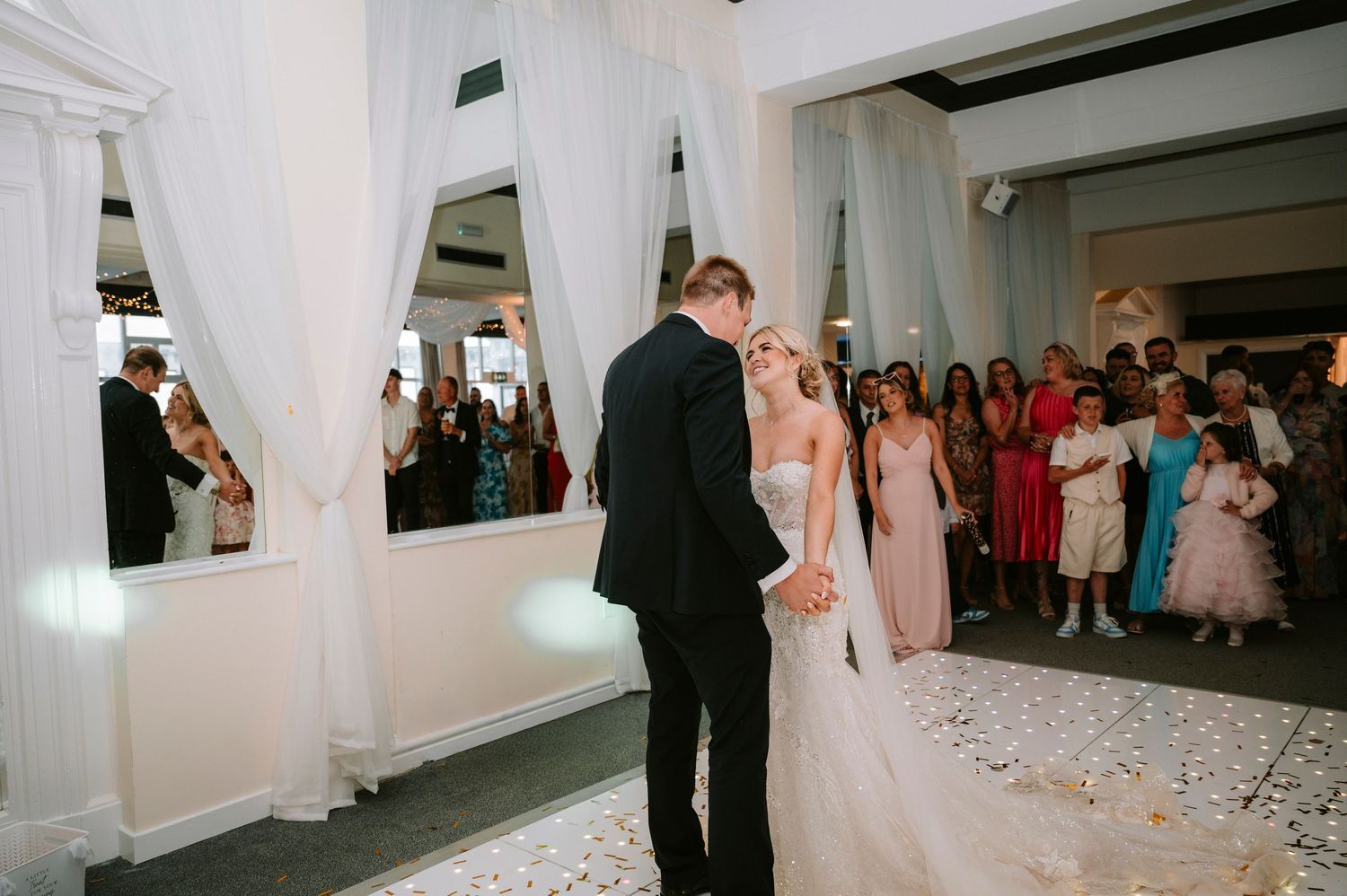 Wedding guests watch the newlyweds dance in a white-draped reception hall.