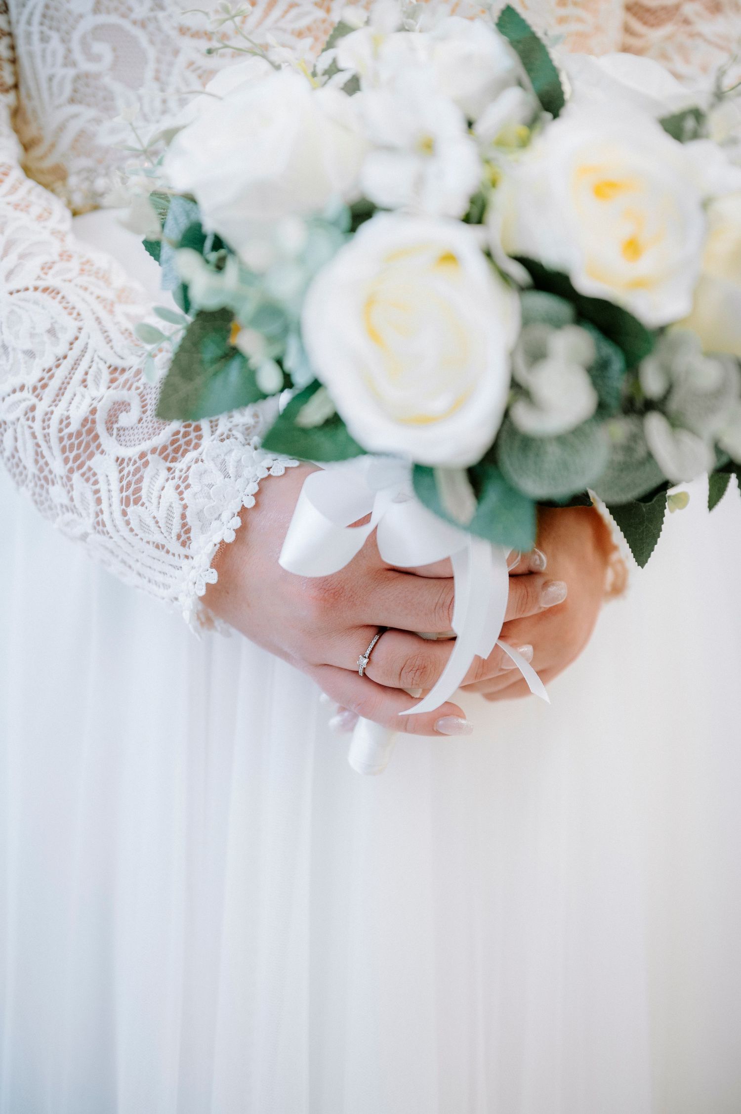 Close-up of hands holding an elegant white rose and peony bridal bouquet with green foliage.