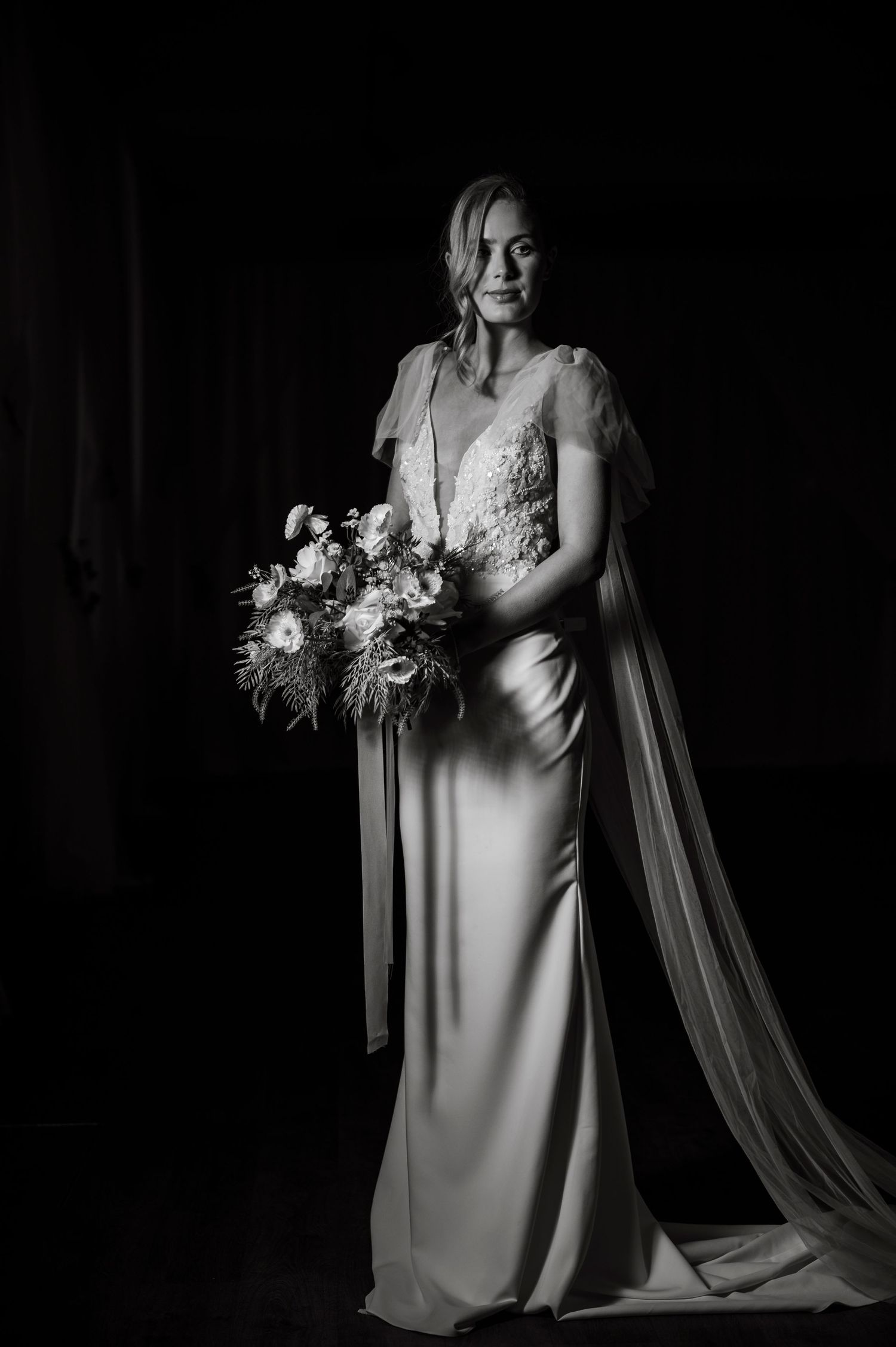 Dramatic black and white bridal portrait with flowing veil and floral bouquet.