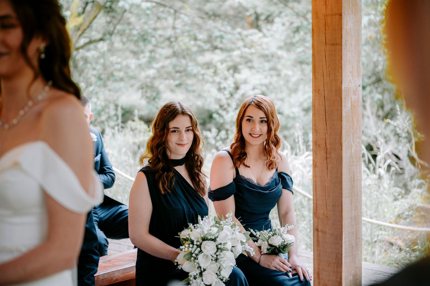 Wedding party in navy and white attire standing in rustic outdoor pavilion.