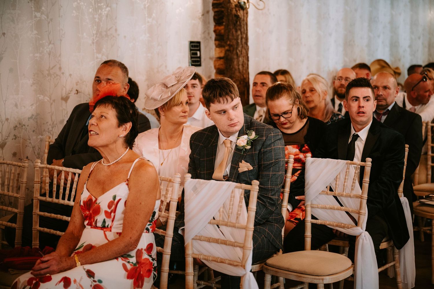 Wedding ceremony guests seated in rows watching attentively in a warm-lit indoor venue.