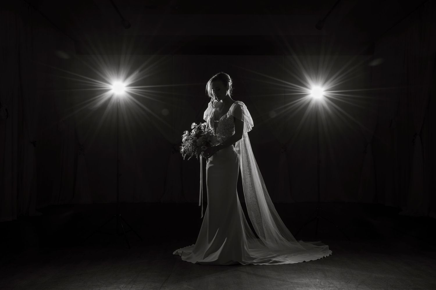 Dramatic spotlit wedding photography with silhouettes against dark background.
