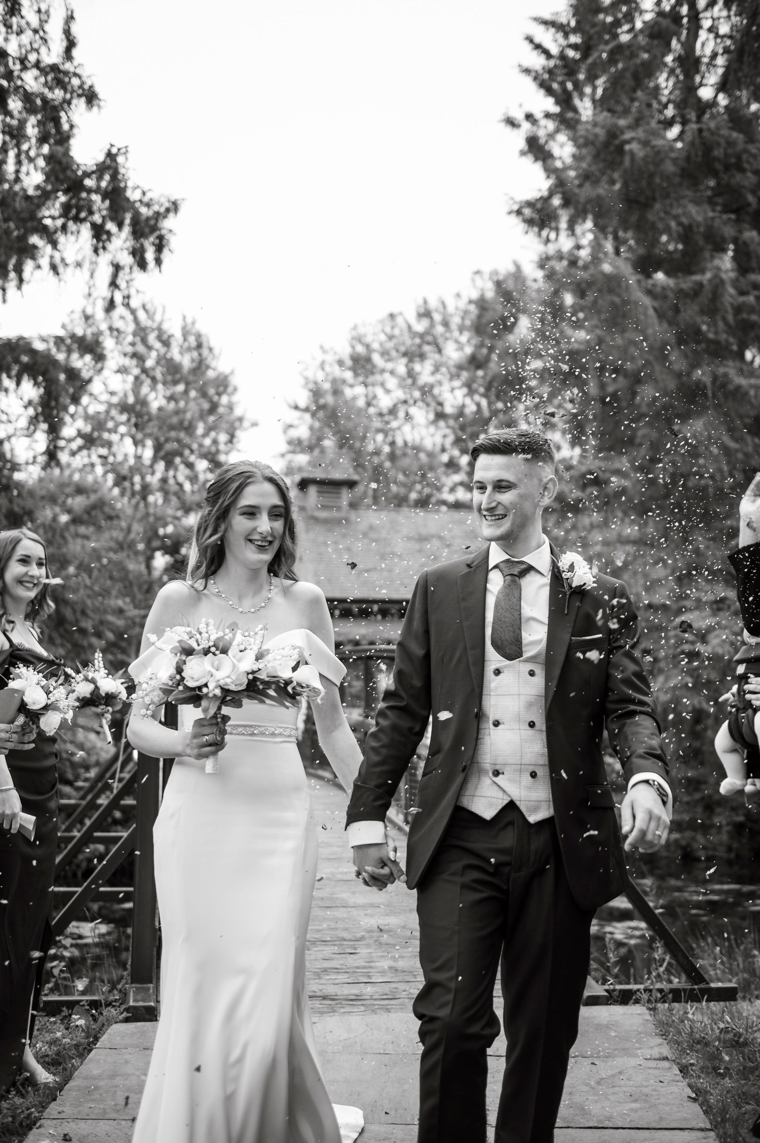 Black and white portrait of newlyweds celebrating outdoors with confetti.