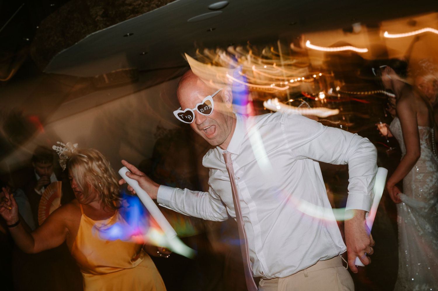 Wedding guests dance and celebrate on a dimly lit dance floor during the reception.